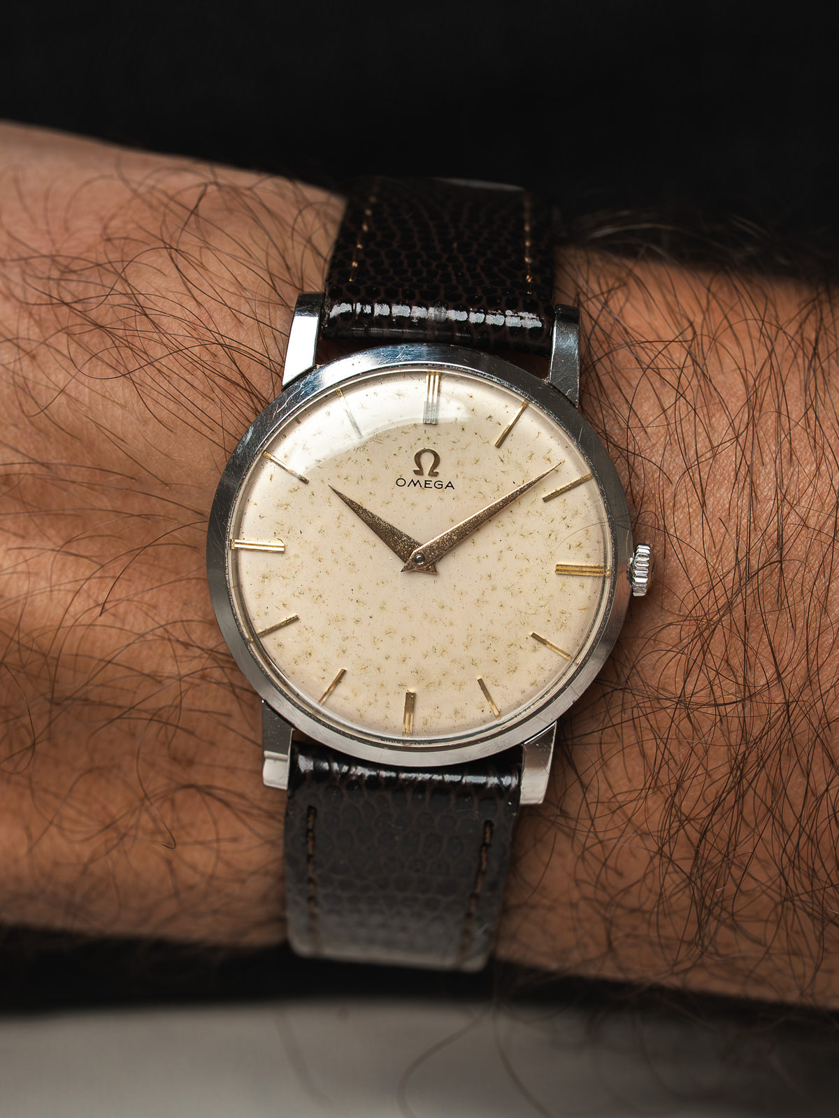 Montre Omega vintage au cadran crème et bracelet cuir noir, portée au poignet