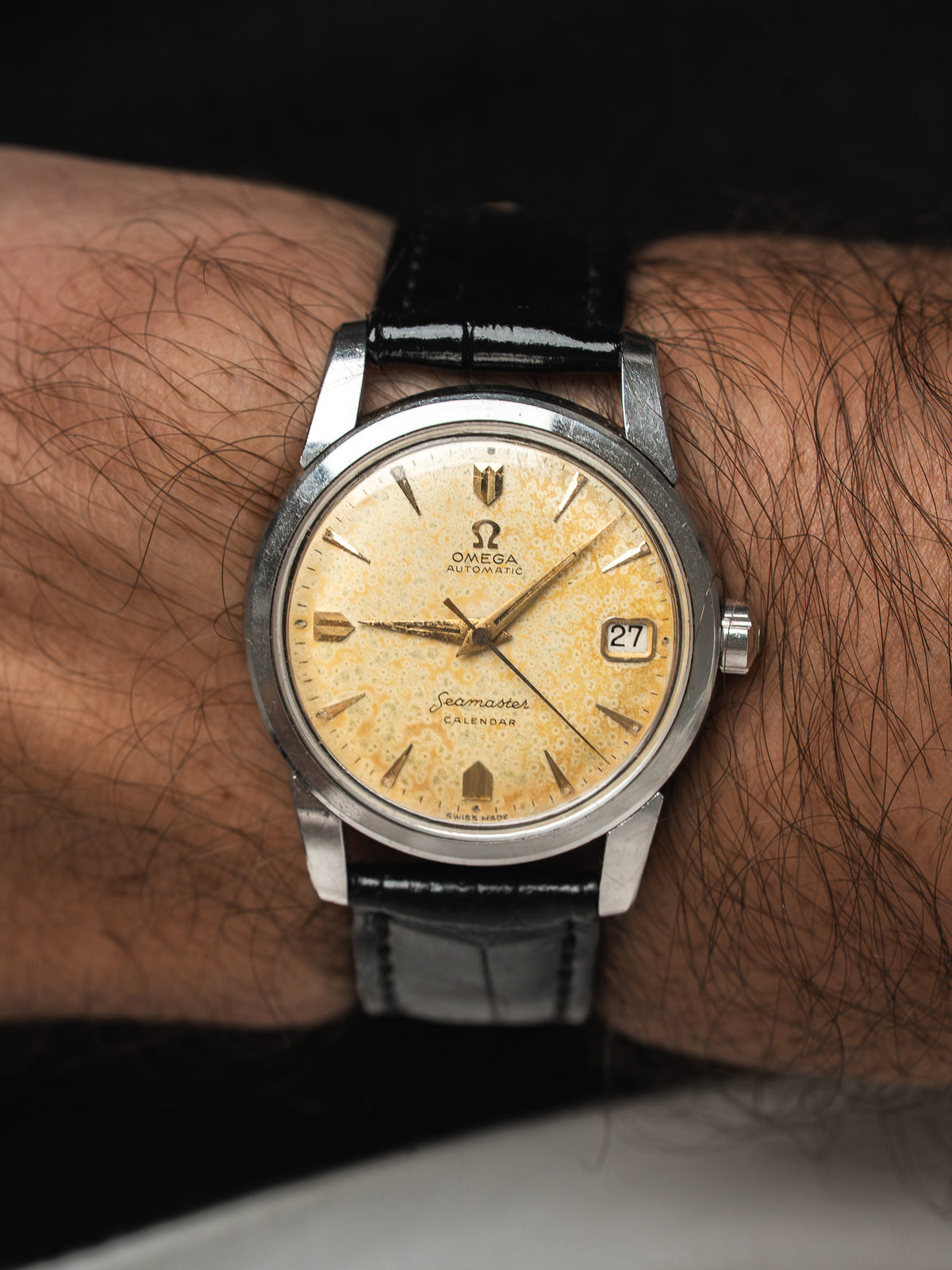 Montre Omega Seamaster vintage en acier, cadran patiné et bracelet cuir noir au poignet