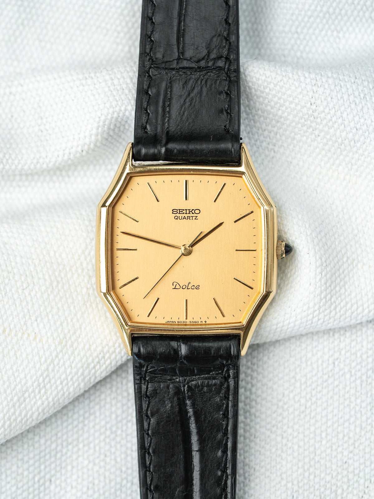 Montre Seiko Dolce vintage avec boîtier doré, cadran champagne et bracelet en cuir noir.