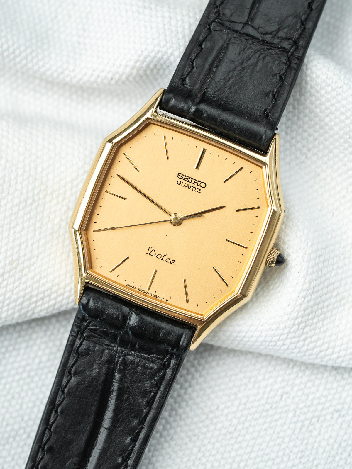 Montre Seiko Dolce vintage au boîtier doré hexagonal et bracelet en cuir noir.