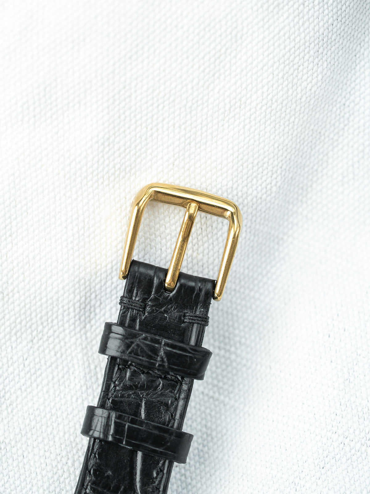 Détail d'une boucle dorée sur un bracelet de montre en cuir noir grainé.