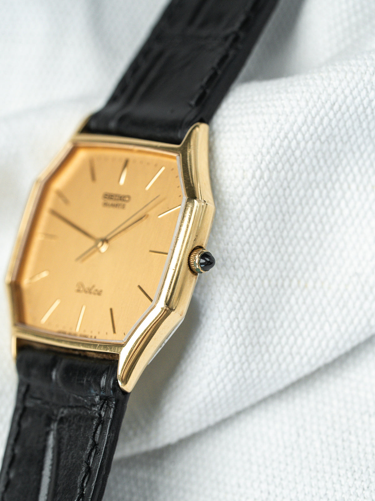 Montre Seiko Dolce vintage avec boîtier doré, cadran doré et bracelet en cuir noir.