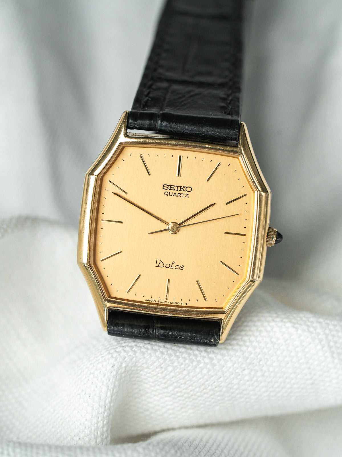 Montre Seiko Dolce vintage avec cadran doré, boîtier octogonal et bracelet en cuir noir.