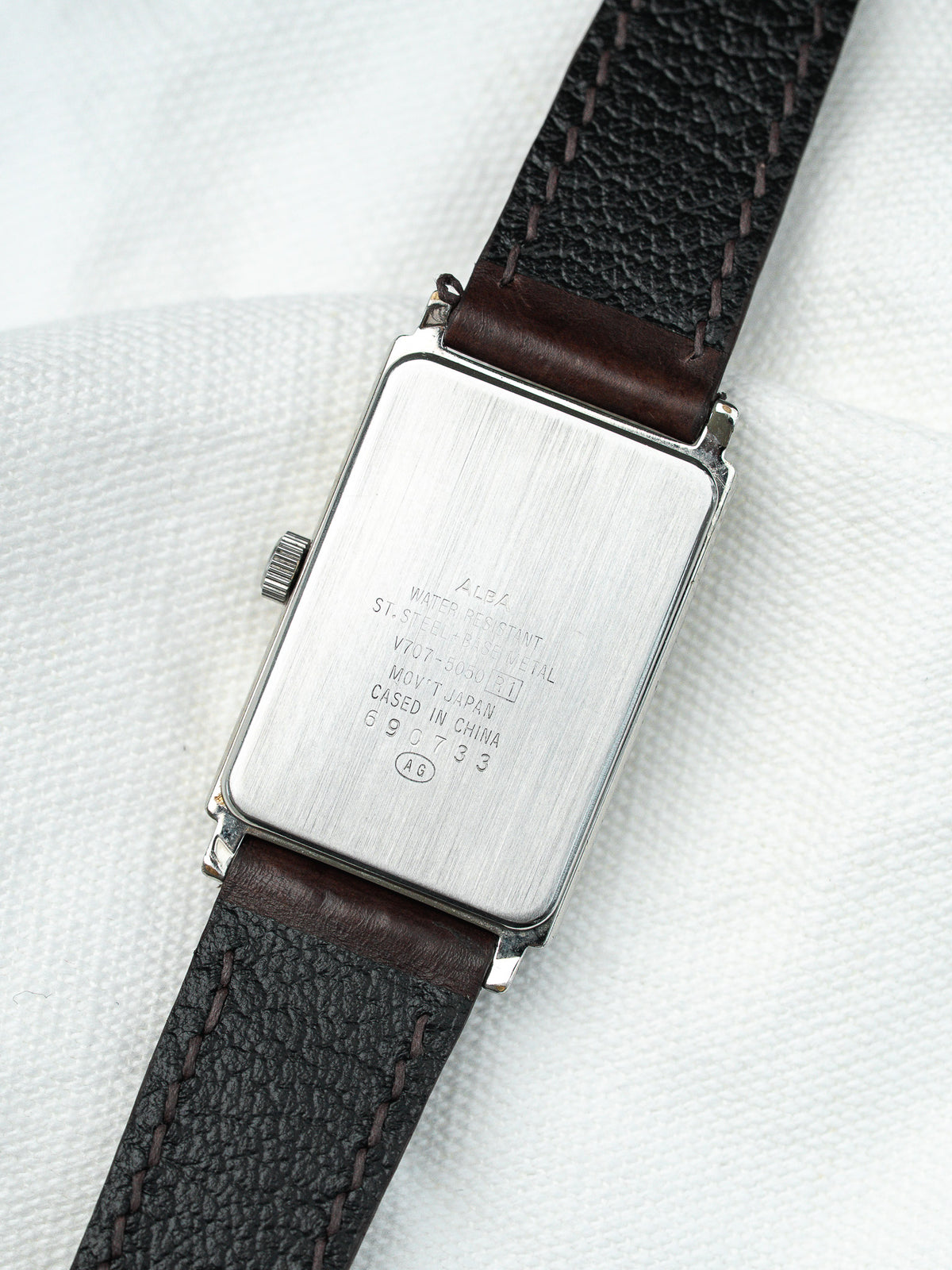 Dos d'une montre rectangulaire en acier avec un bracelet en cuir noir grainé.