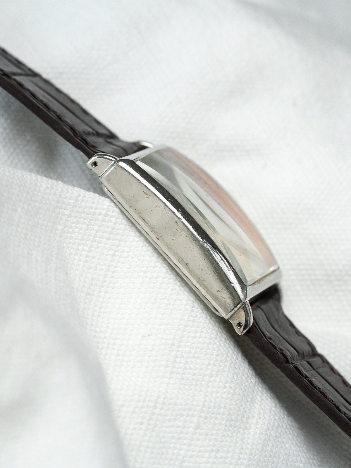 Montre vintage rectangulaire en acier avec bracelet en cuir marron sur tissu blanc.