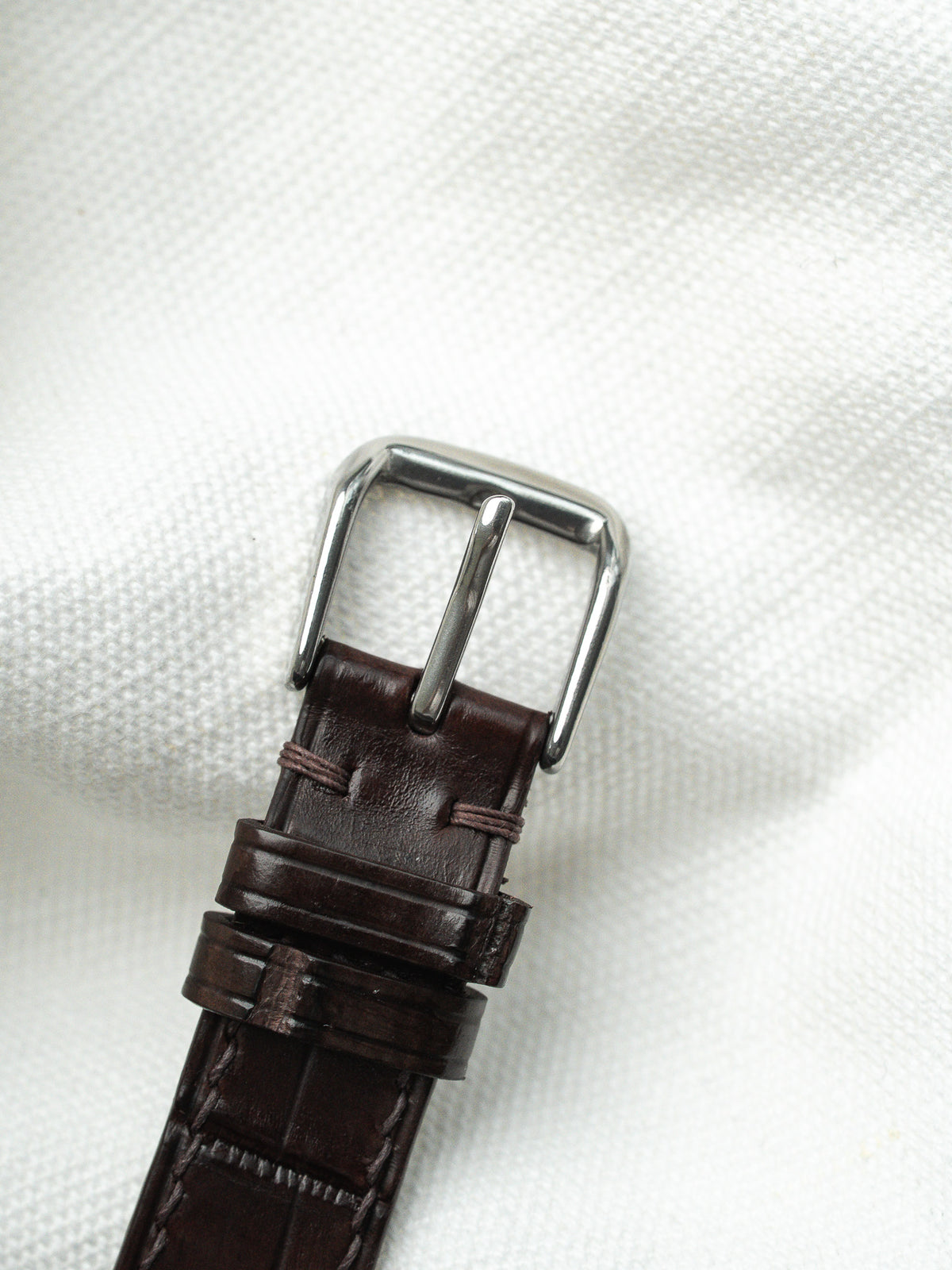 Boucle ardillon argentée et bracelet en cuir marron foncé sur fond blanc.