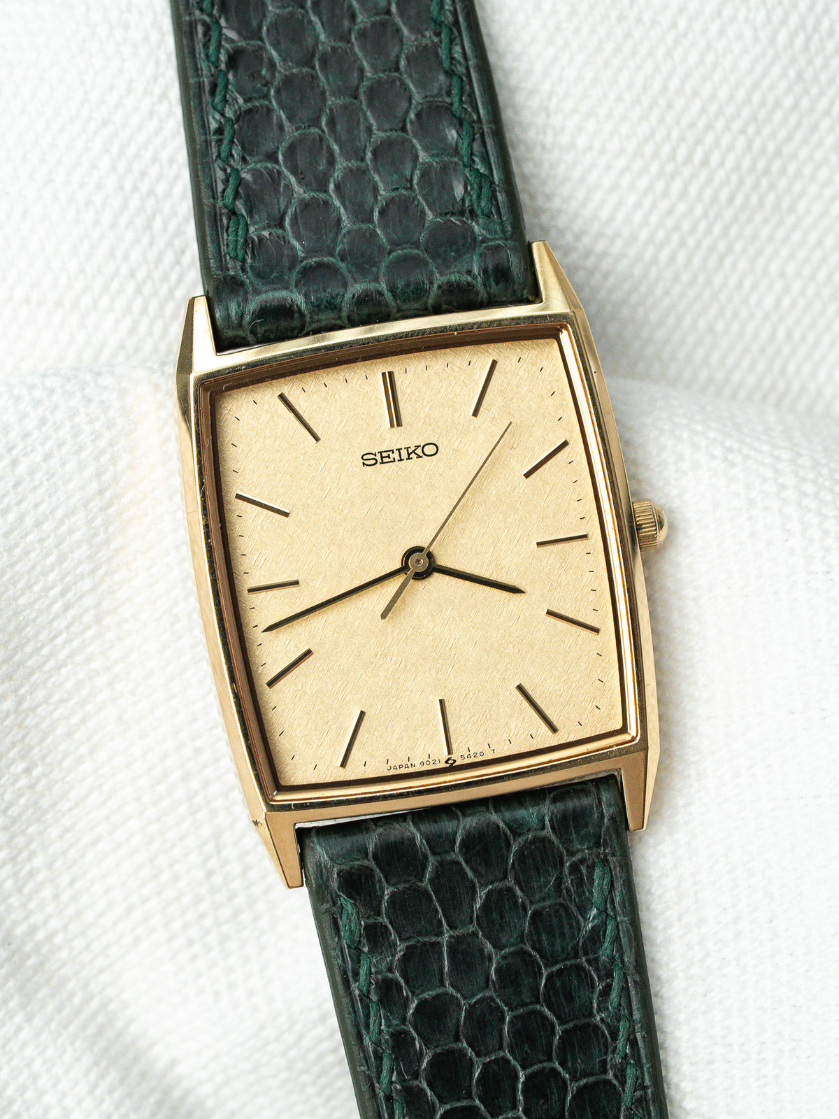 Montre Seiko vintage au boîtier doré rectangulaire et bracelet en cuir vert texturé.