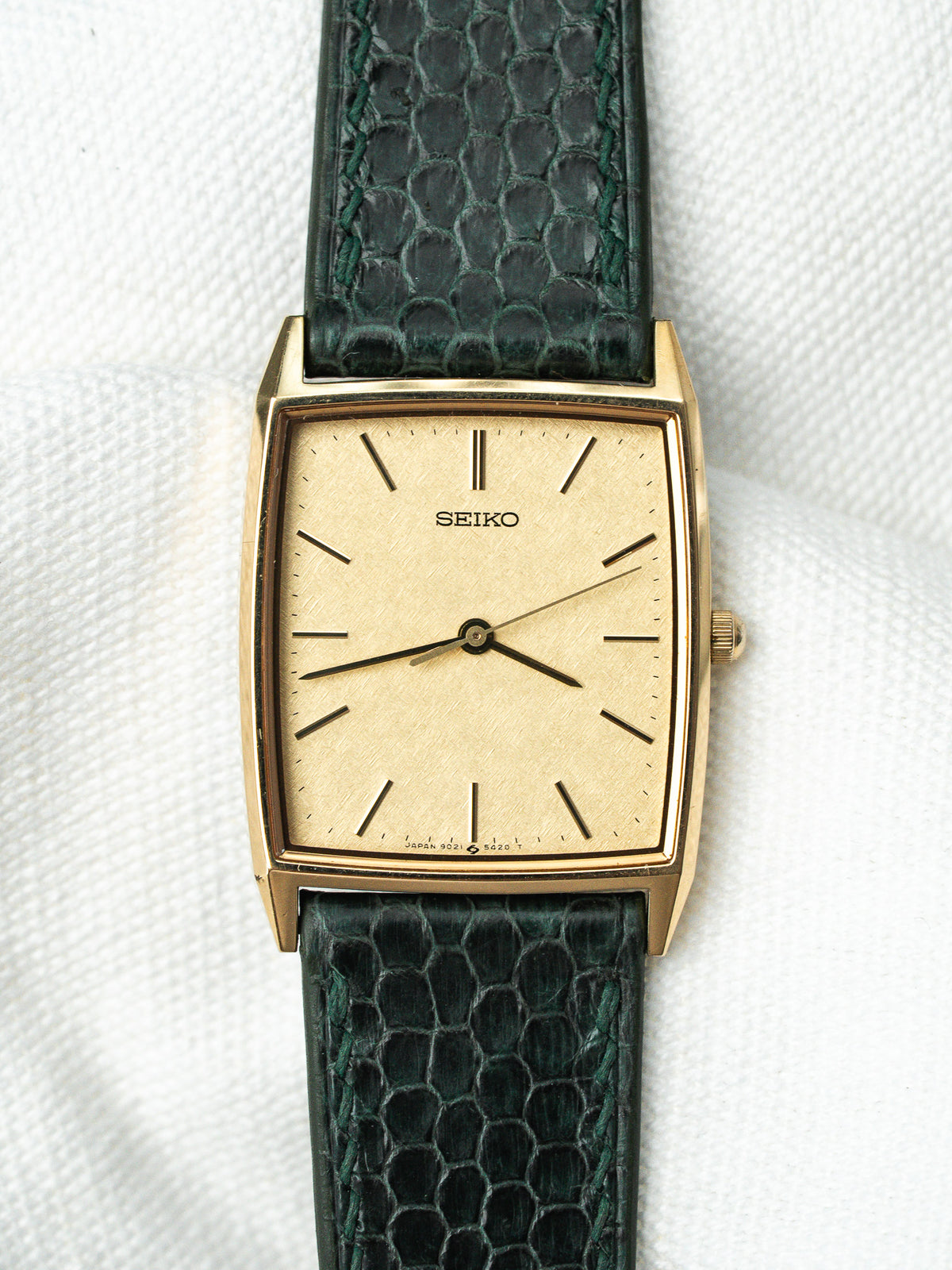Montre Seiko vintage avec boîtier rectangulaire doré, cadran champagne et bracelet en cuir vert.