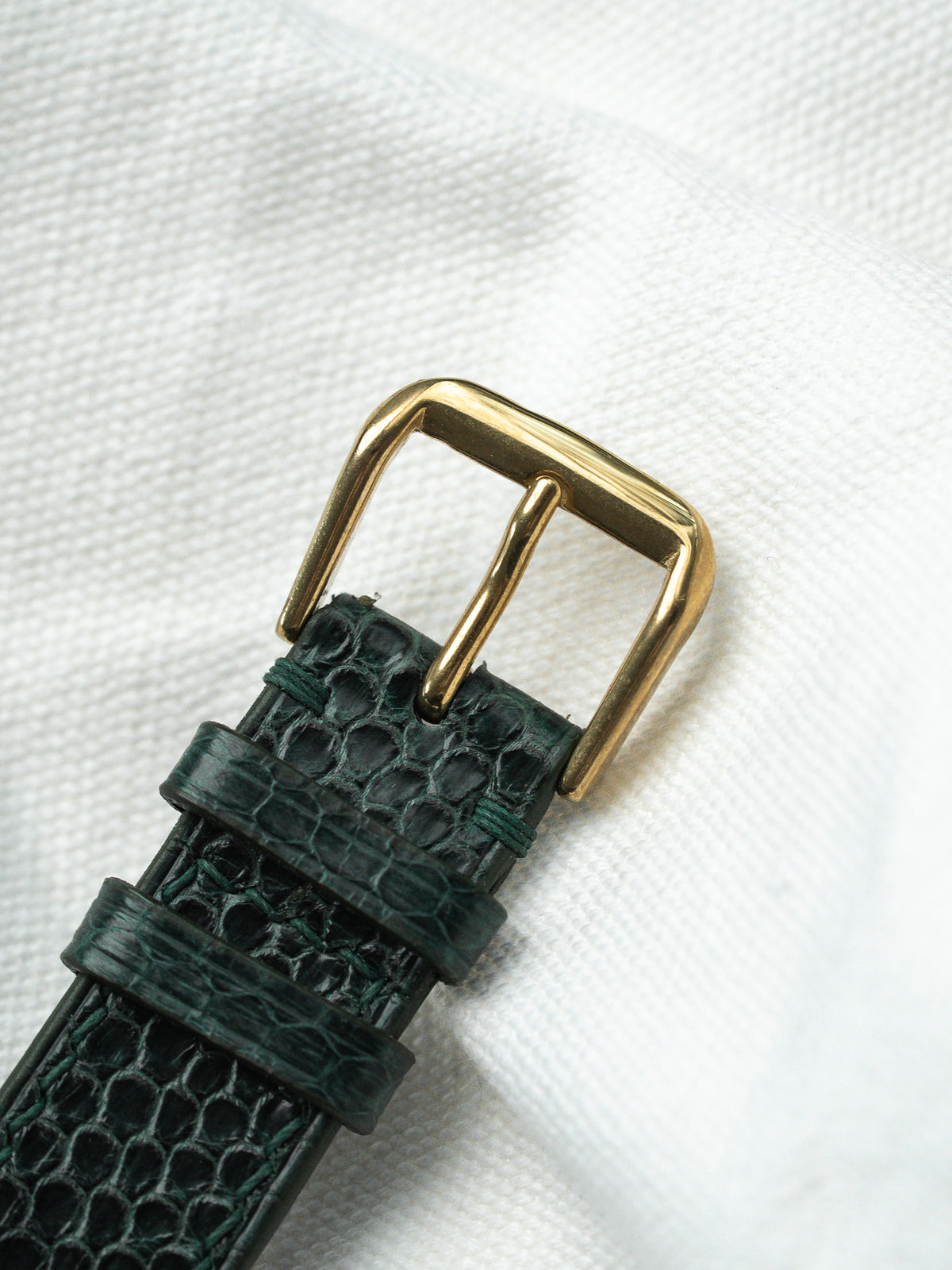 Détail d'un bracelet de montre en cuir vert texturé avec boucle dorée.