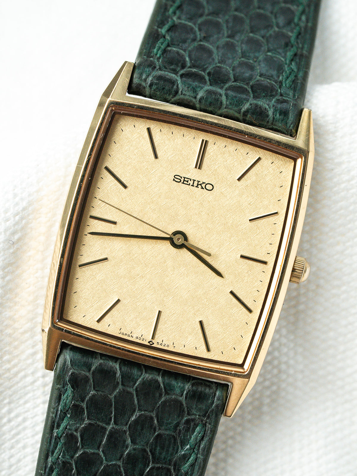 Montre Seiko vintage à boîtier rectangulaire doré et bracelet en cuir vert texturé.