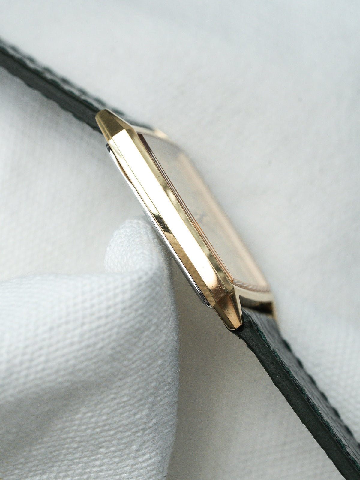 Vue de profil d'une montre au boîtier doré avec un bracelet en cuir vert.