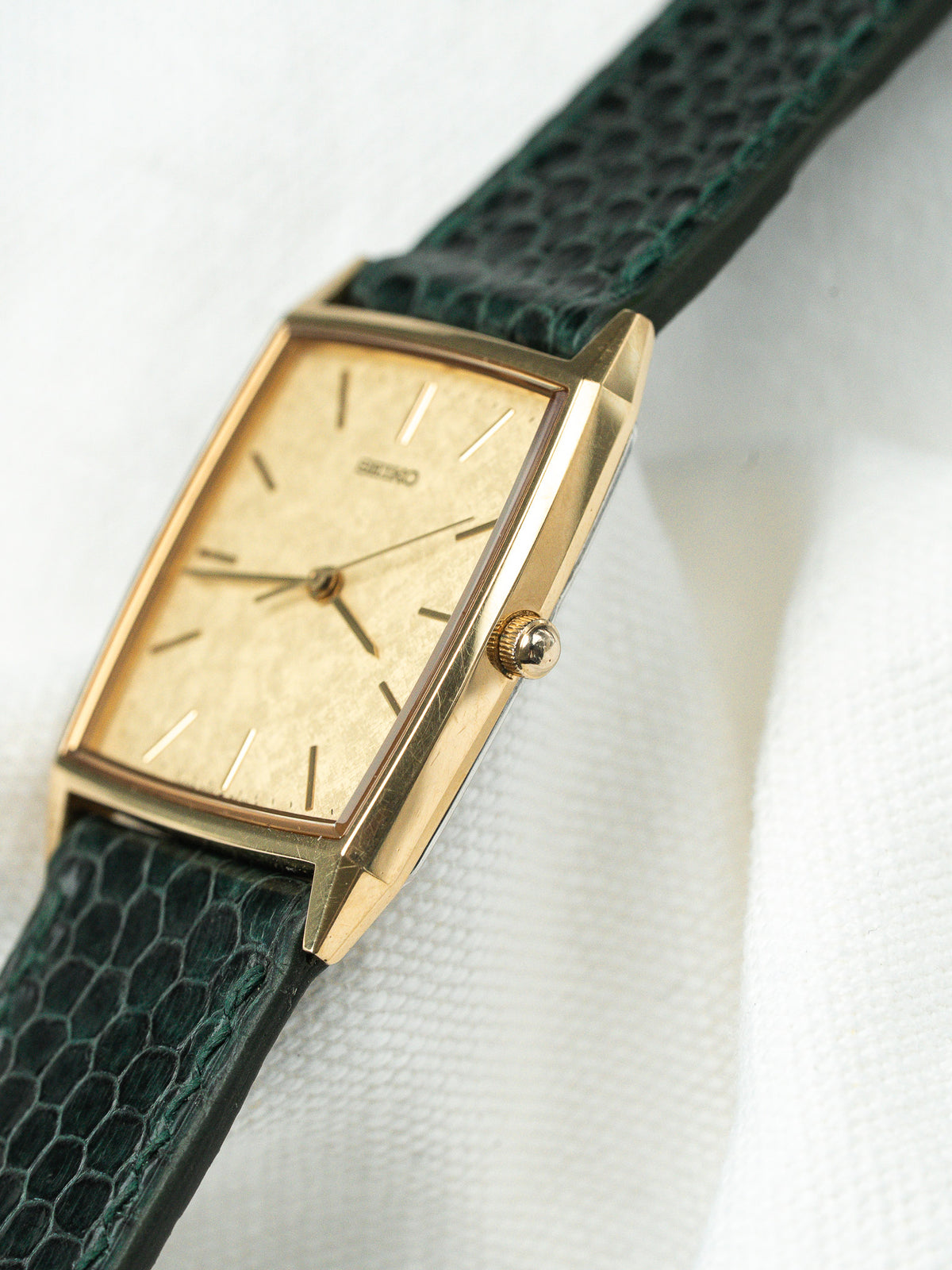 Montre vintage à boîtier rectangulaire doré avec cadran texturé et bracelet en cuir vert.
