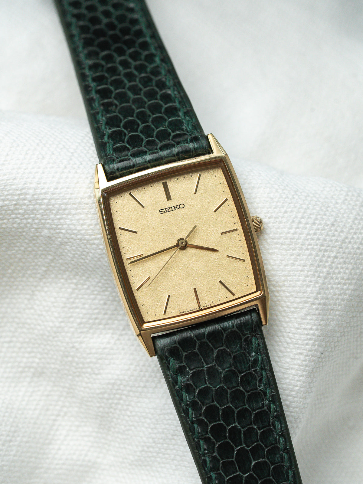 Montre Seiko vintage rectangulaire dorée avec un bracelet en cuir vert texturé.