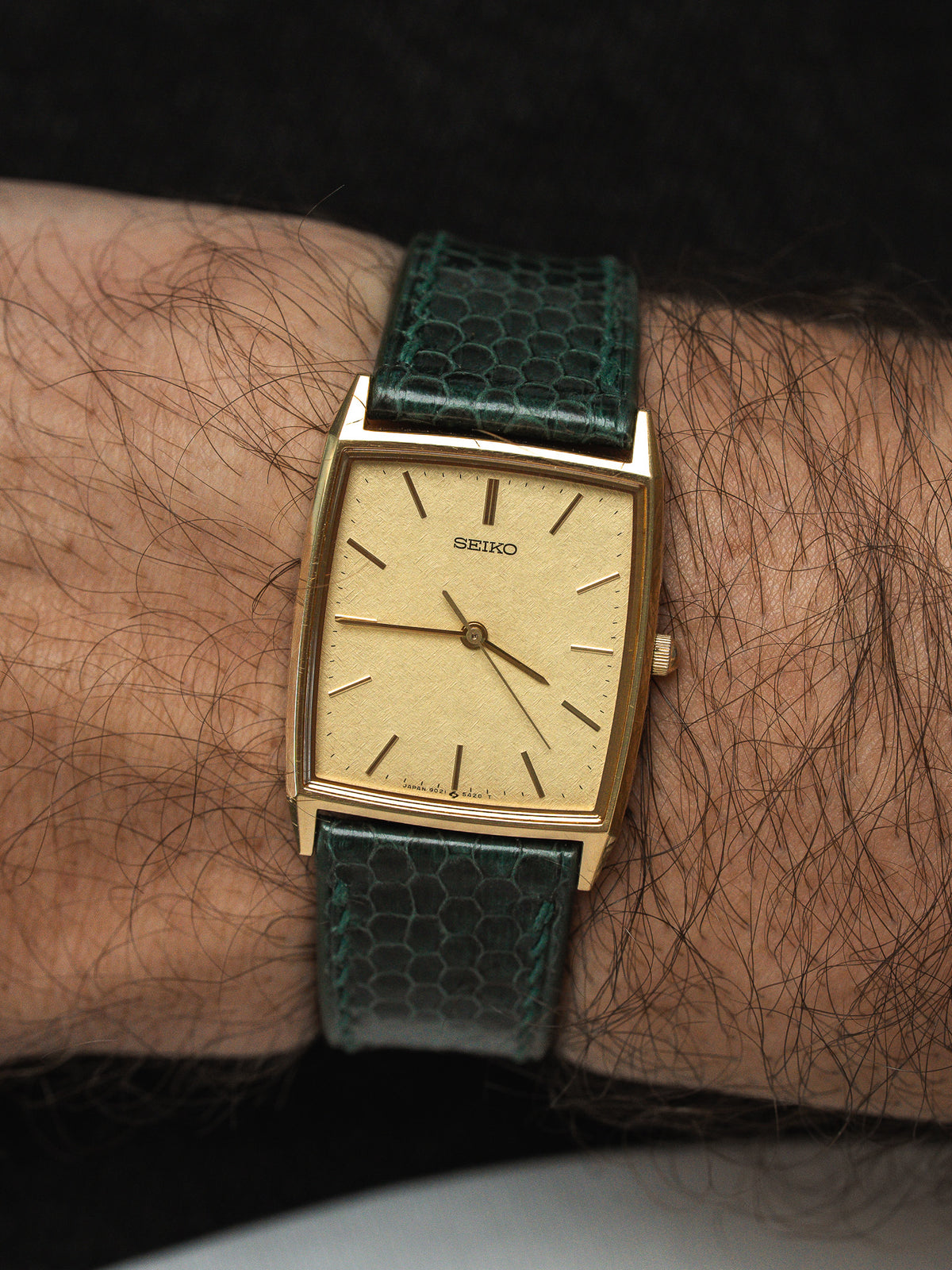 Montre Seiko vintage avec boîtier rectangulaire doré et bracelet en cuir vert texturé.
