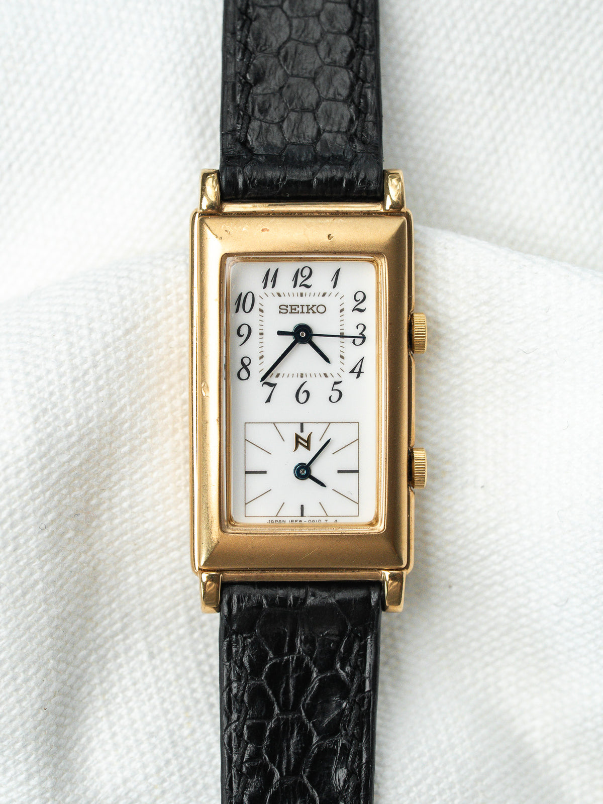 Montre Seiko vintage rectangulaire en or avec cadran blanc et bracelet en cuir noir.