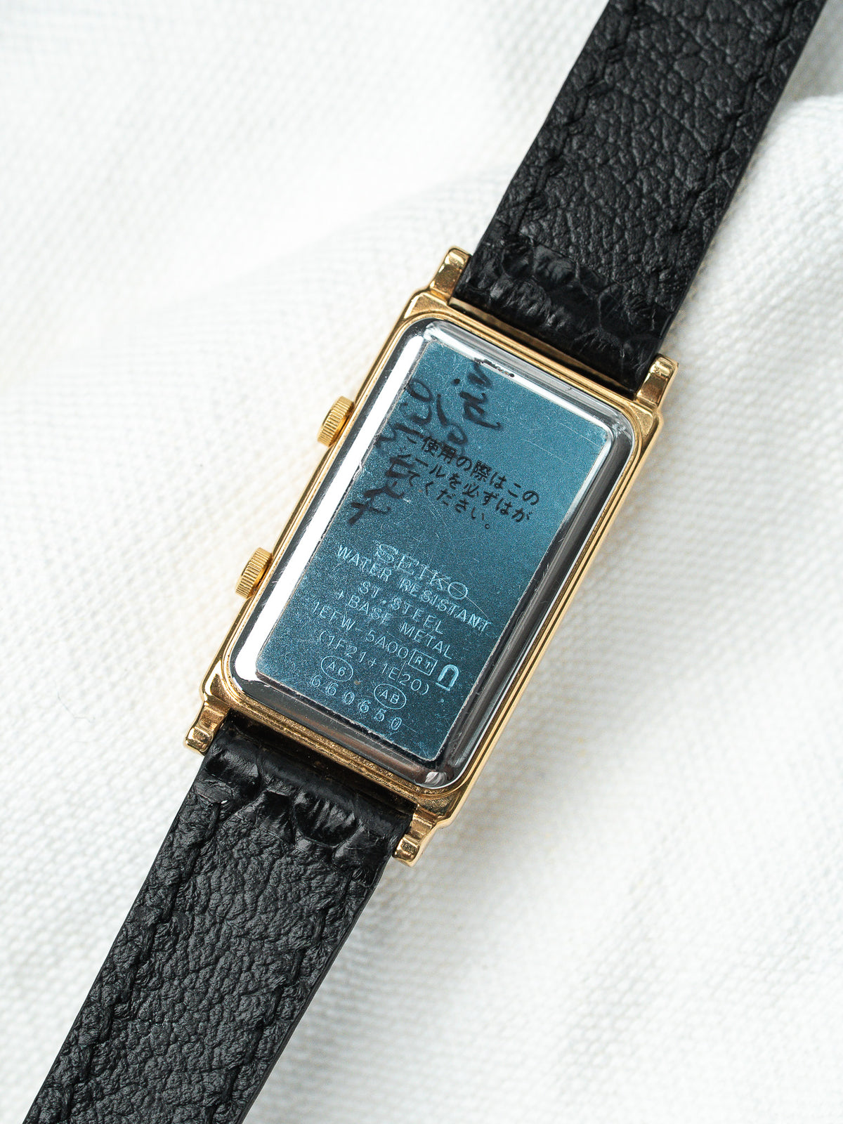 Dos du boîtier d'une montre Seiko en acier doré avec bracelet en cuir noir.