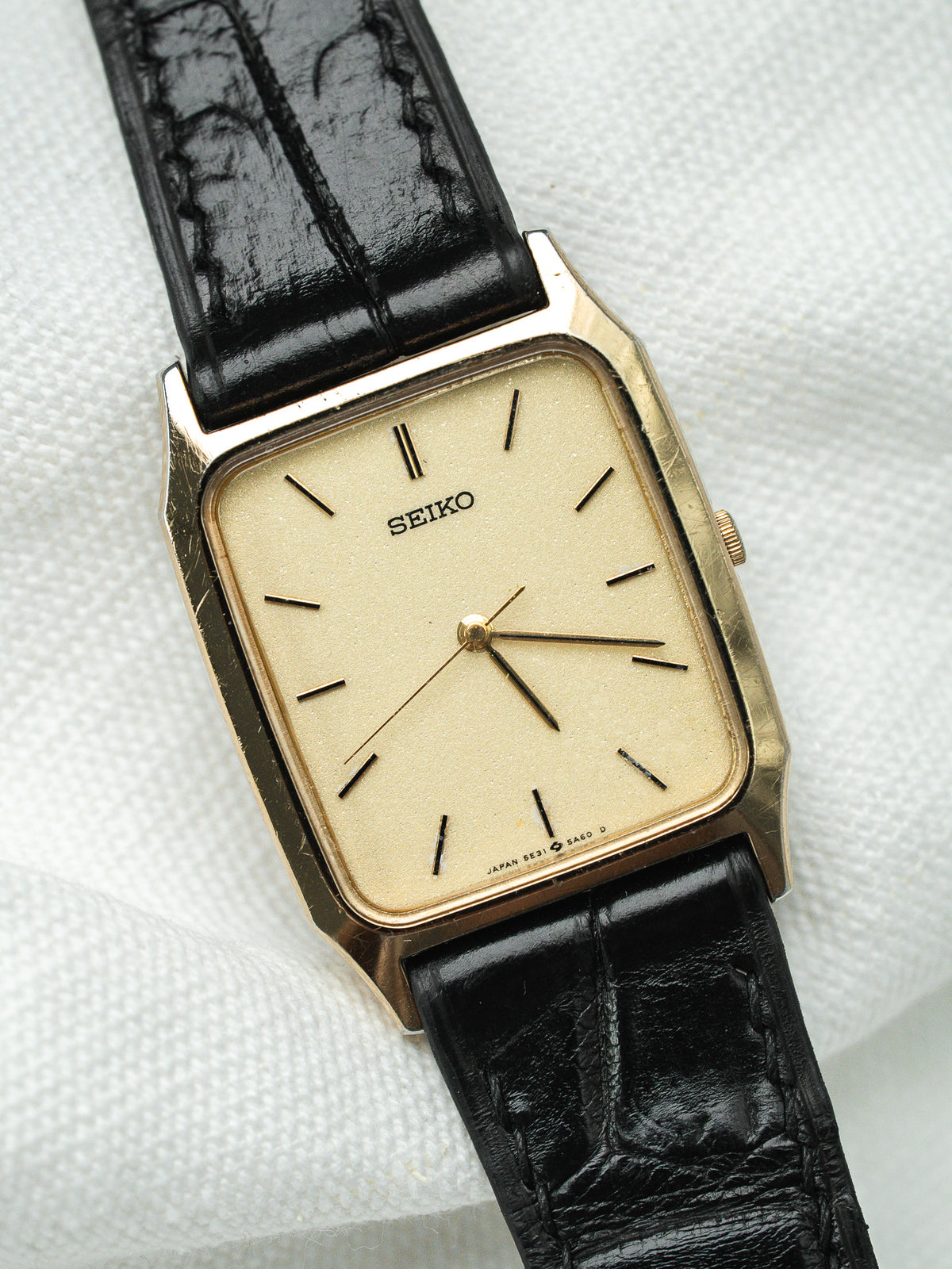 Montre Seiko vintage à boîtier rectangulaire doré, cadran crème et bracelet en cuir noir.