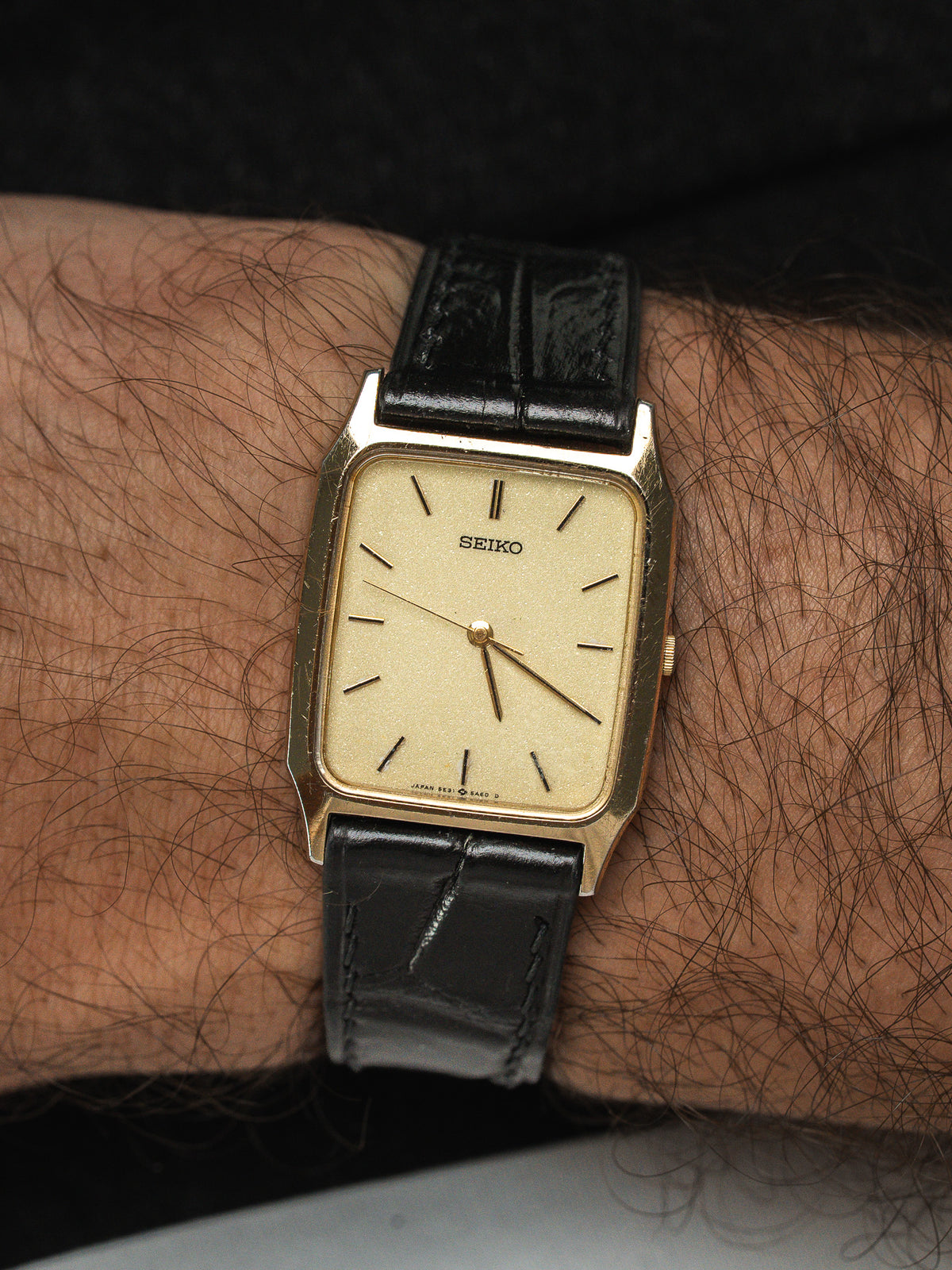 Montre Seiko vintage à boîtier rectangulaire doré et bracelet en cuir noir.