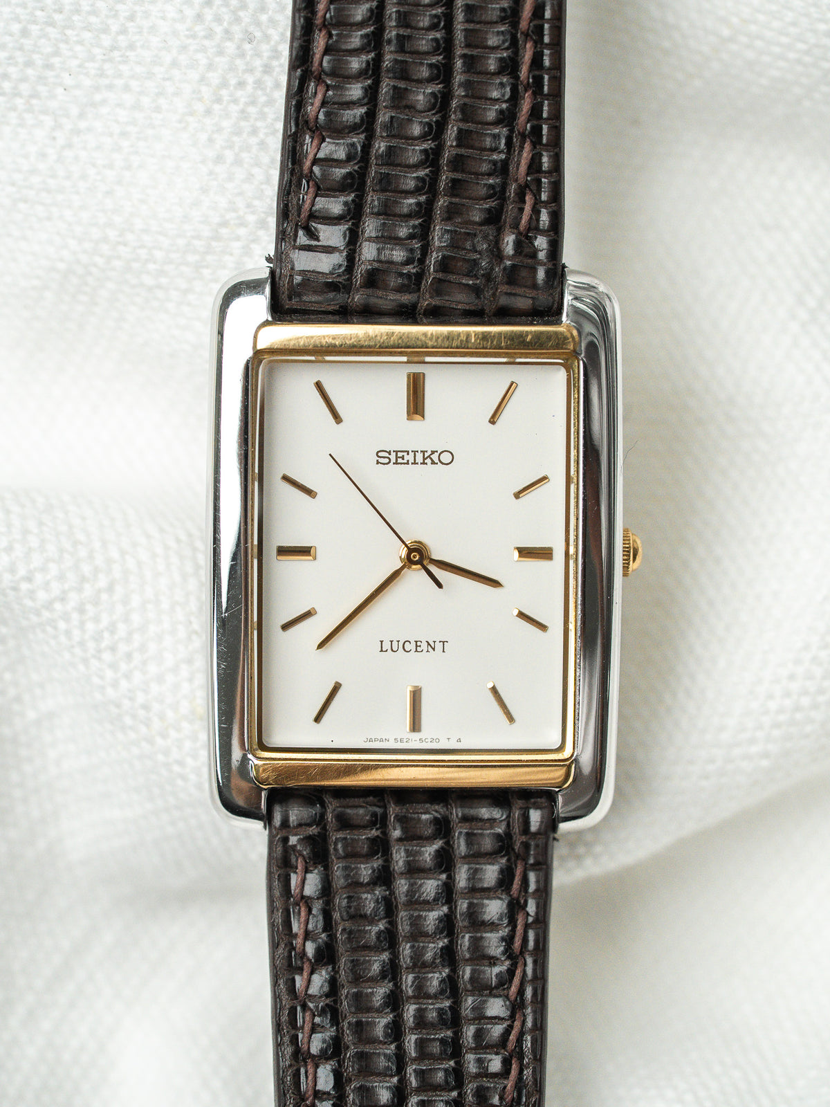 Montre Seiko Lucent rectangulaire avec cadran blanc et bracelet en cuir marron texturé.