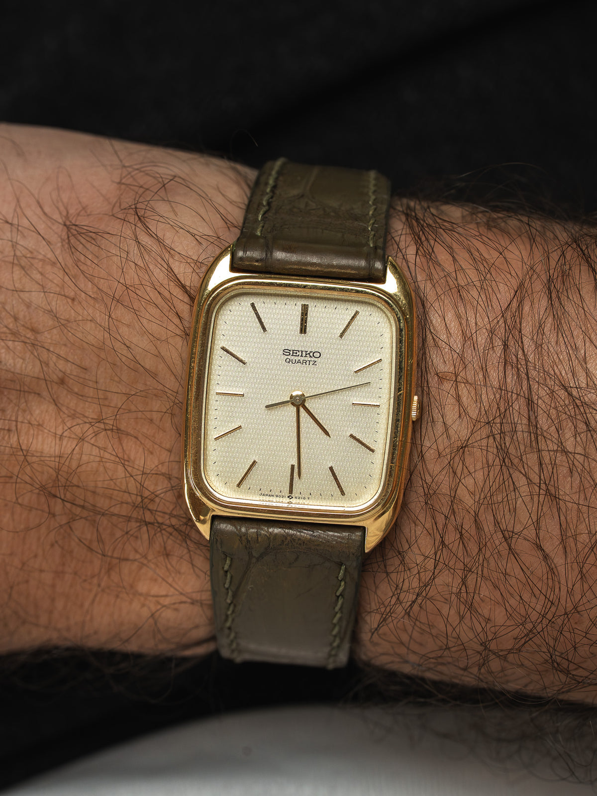 Montre Seiko Quartz vintage à boîtier rectangulaire doré et bracelet en cuir vert.