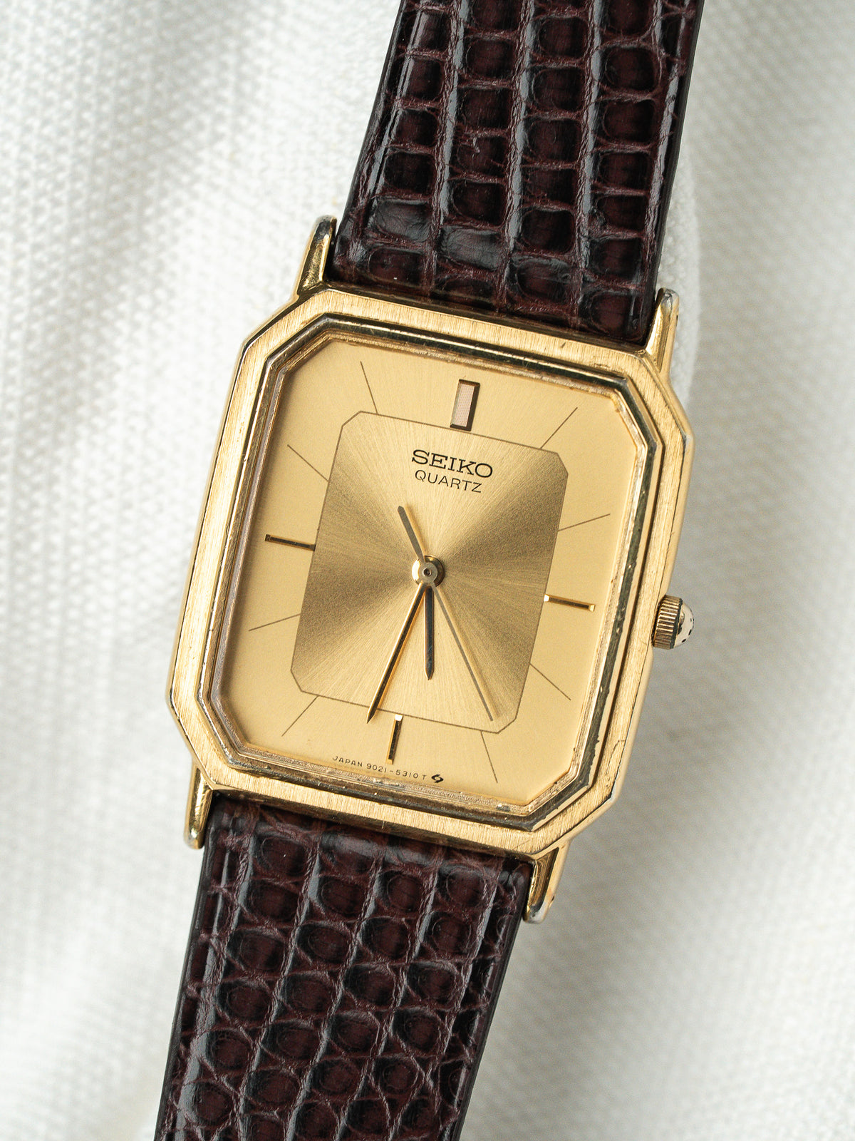Montre Seiko Quartz vintage avec boîtier doré rectangulaire et bracelet en cuir marron.