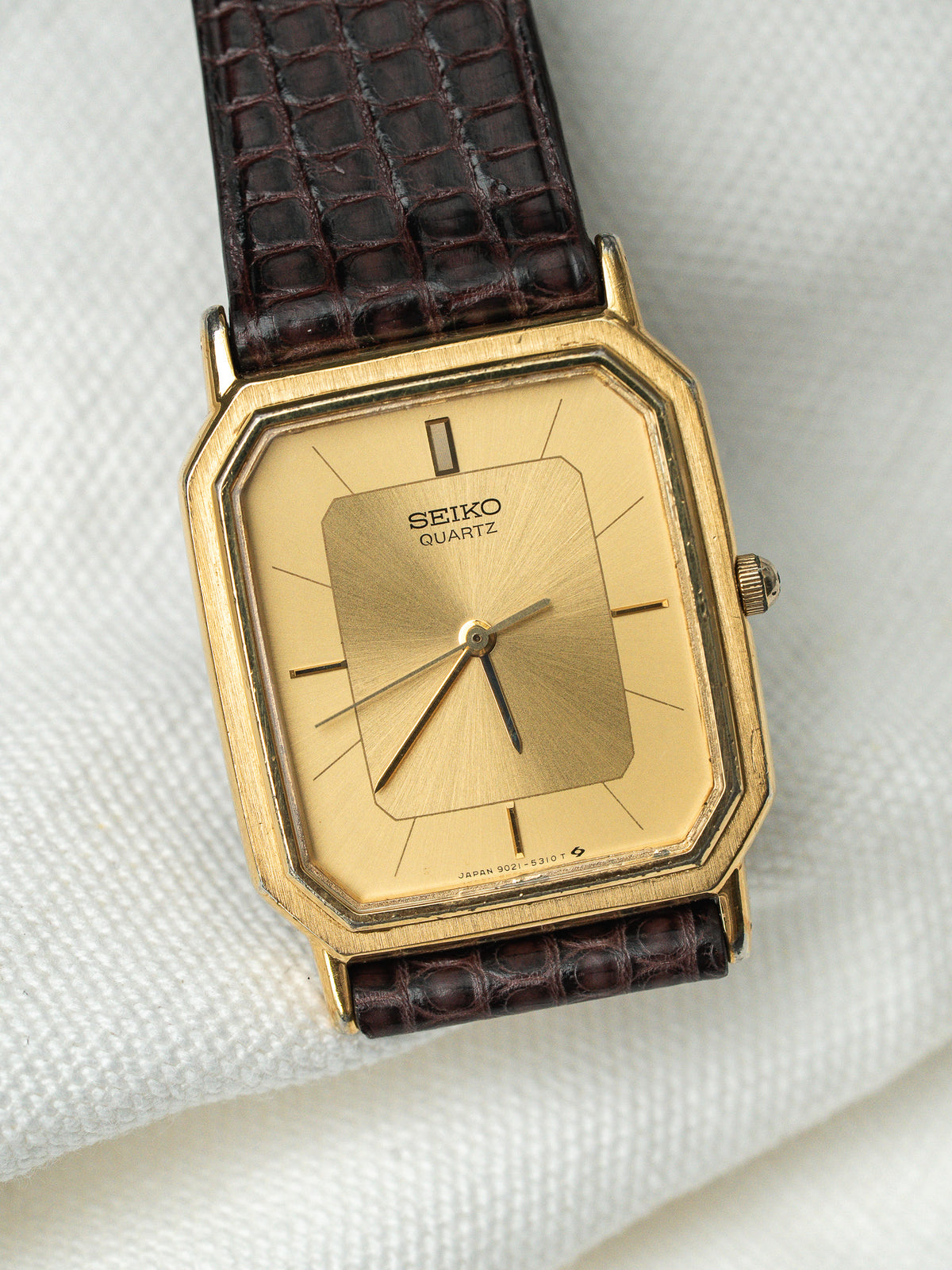 Montre Seiko Quartz vintage avec boîtier doré rectangulaire et bracelet en cuir marron.