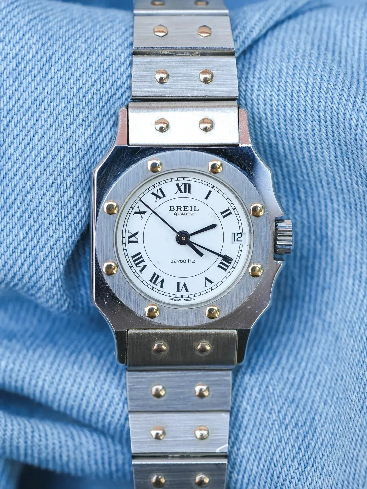 Breil Quartz vintage watch with white dial, Roman numerals, and steel bracelet on blue fabric