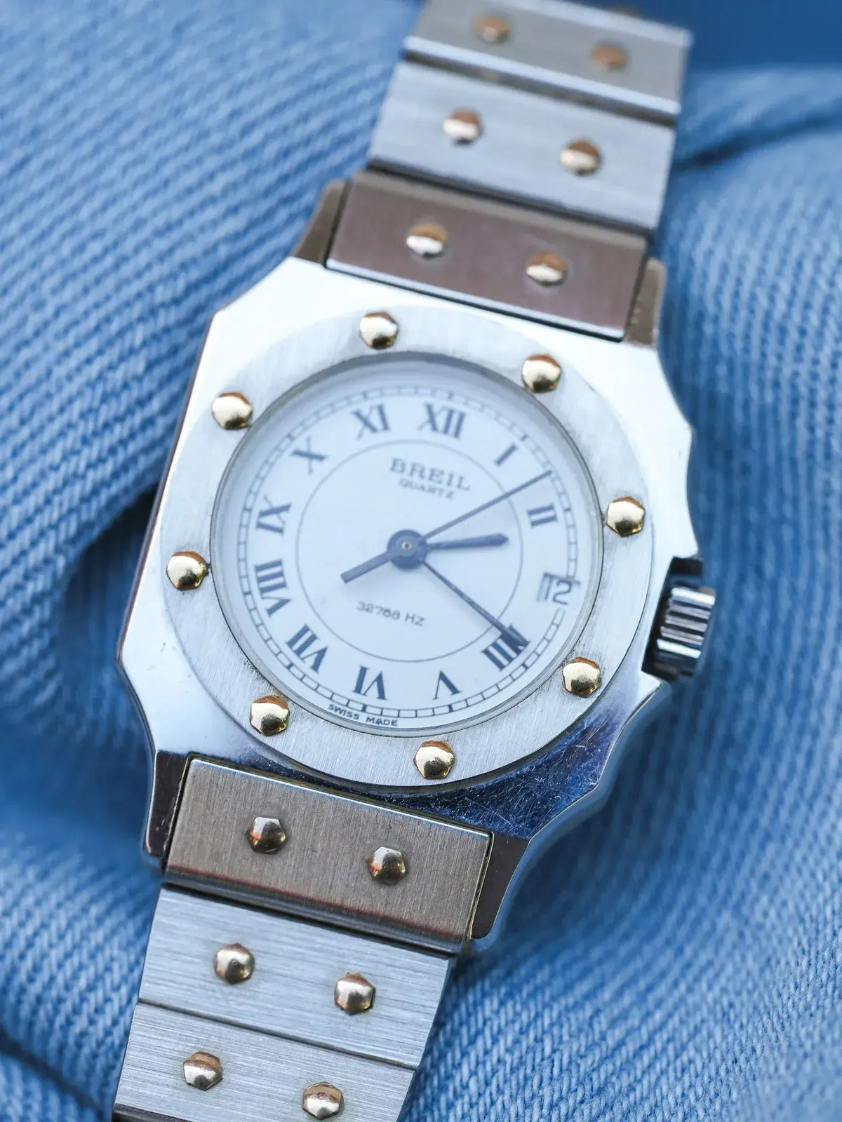 Breil quartz watch with silver case, white dial, Roman numerals, and metal bracelet on blue fabric