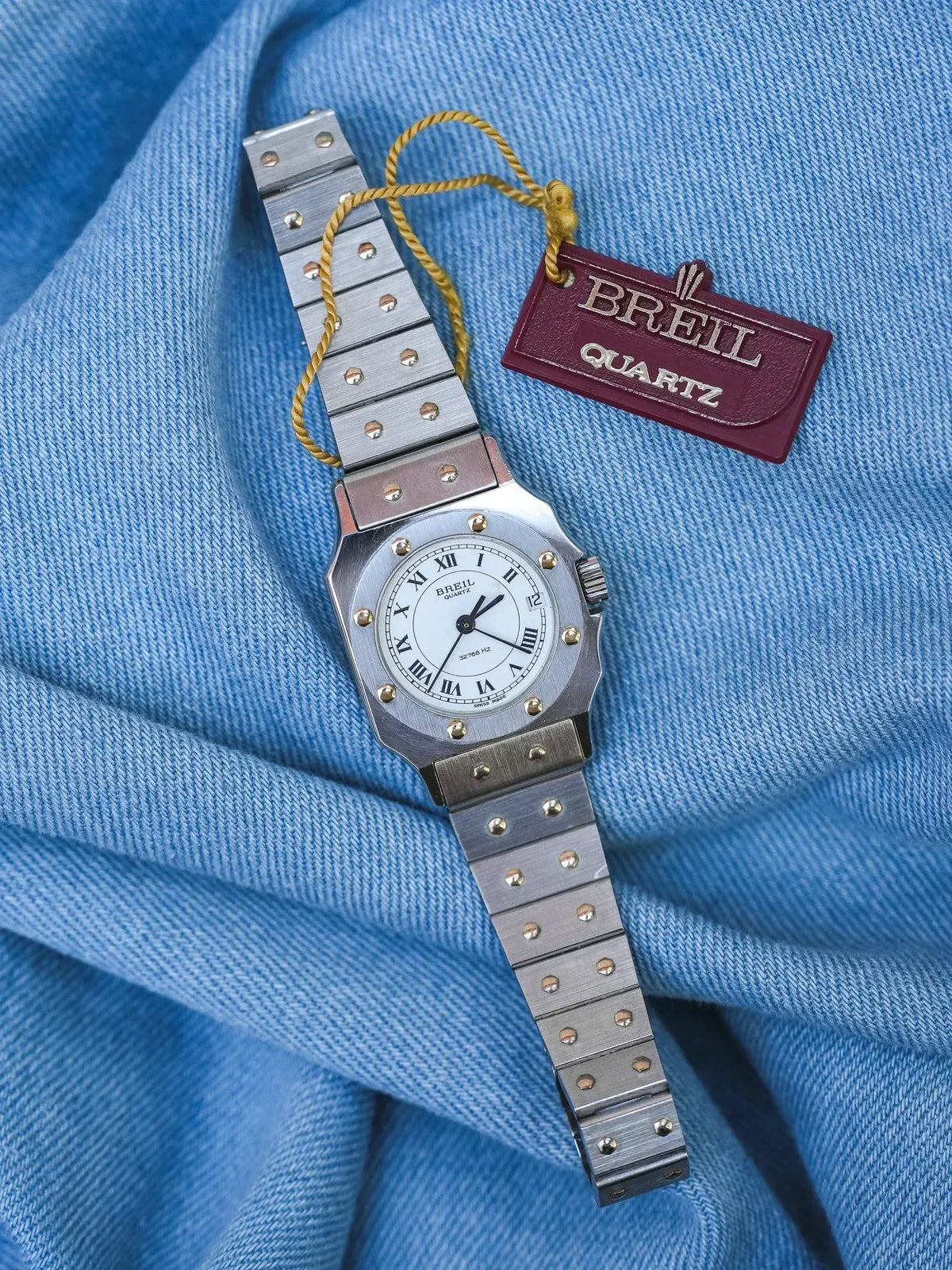Breil Quartz vintage watch with white dial, Roman numerals, and steel bracelet on blue fabric