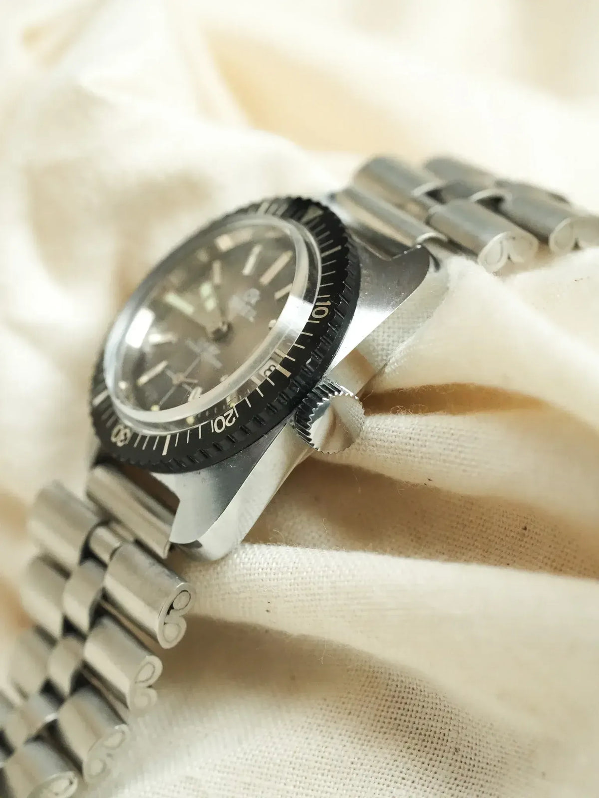 Omega vintage diver watch with black bezel, steel bracelet, resting on cream fabric