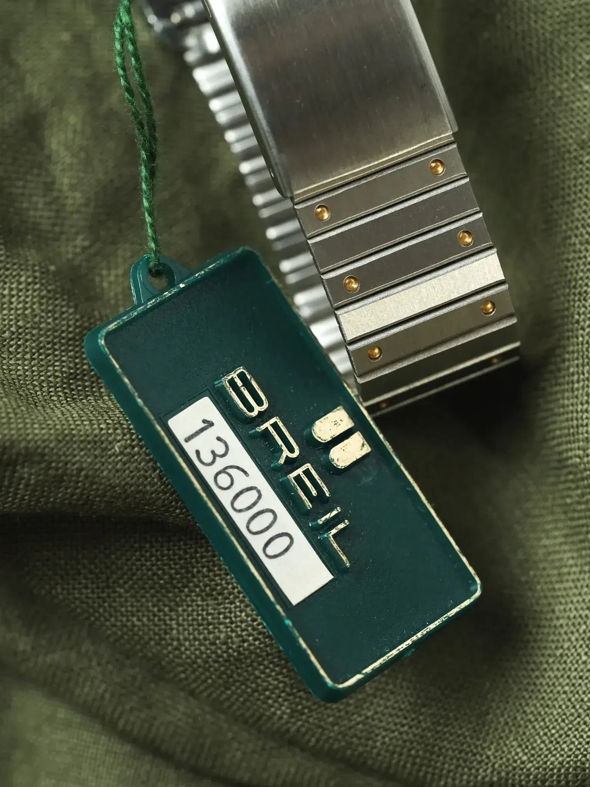Seiko vintage watch tag with model 136000, metal bracelet on olive fabric