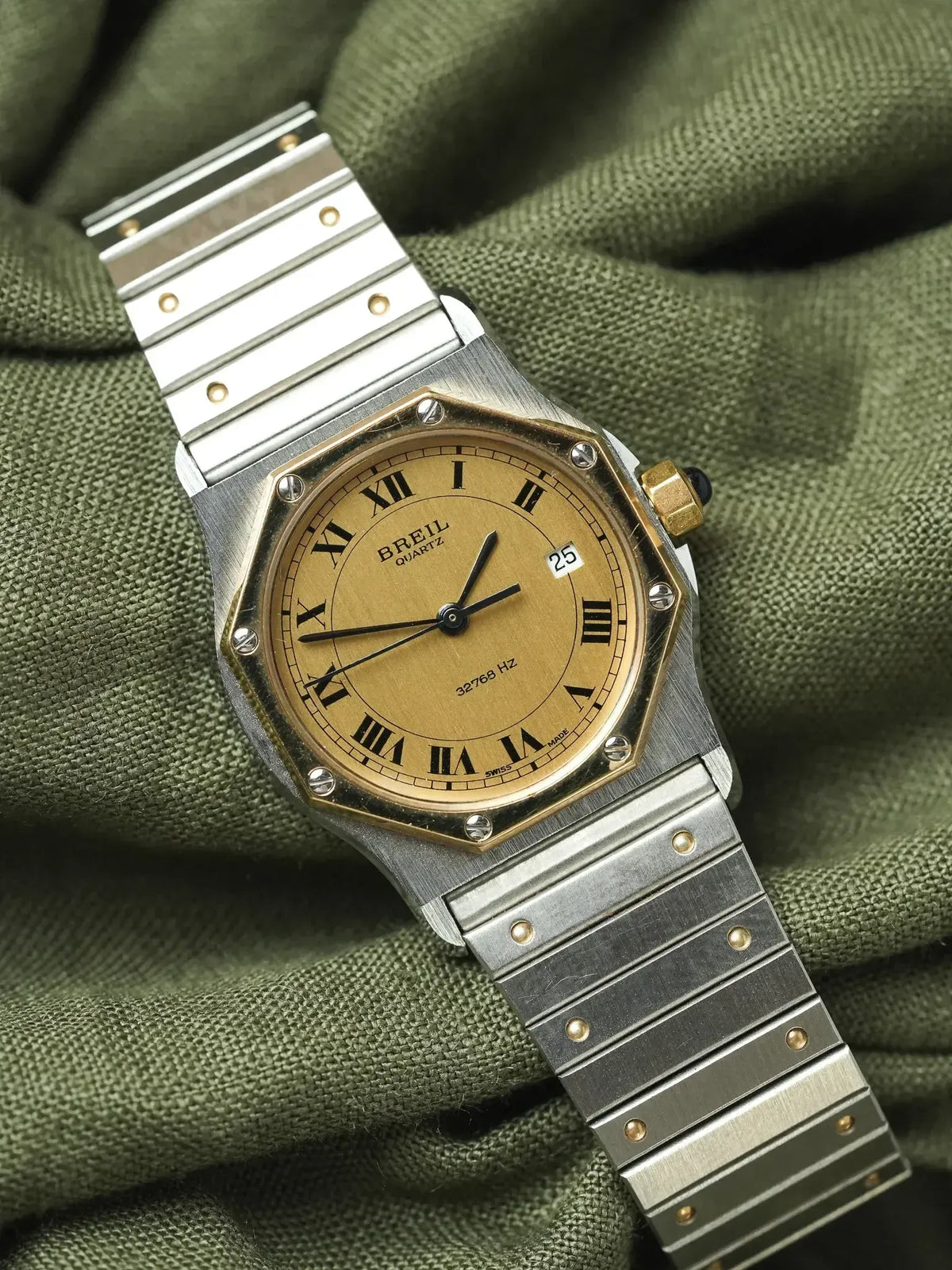 Breil quartz watch with gold dial, Roman numerals, and two-tone steel bracelet on green fabric