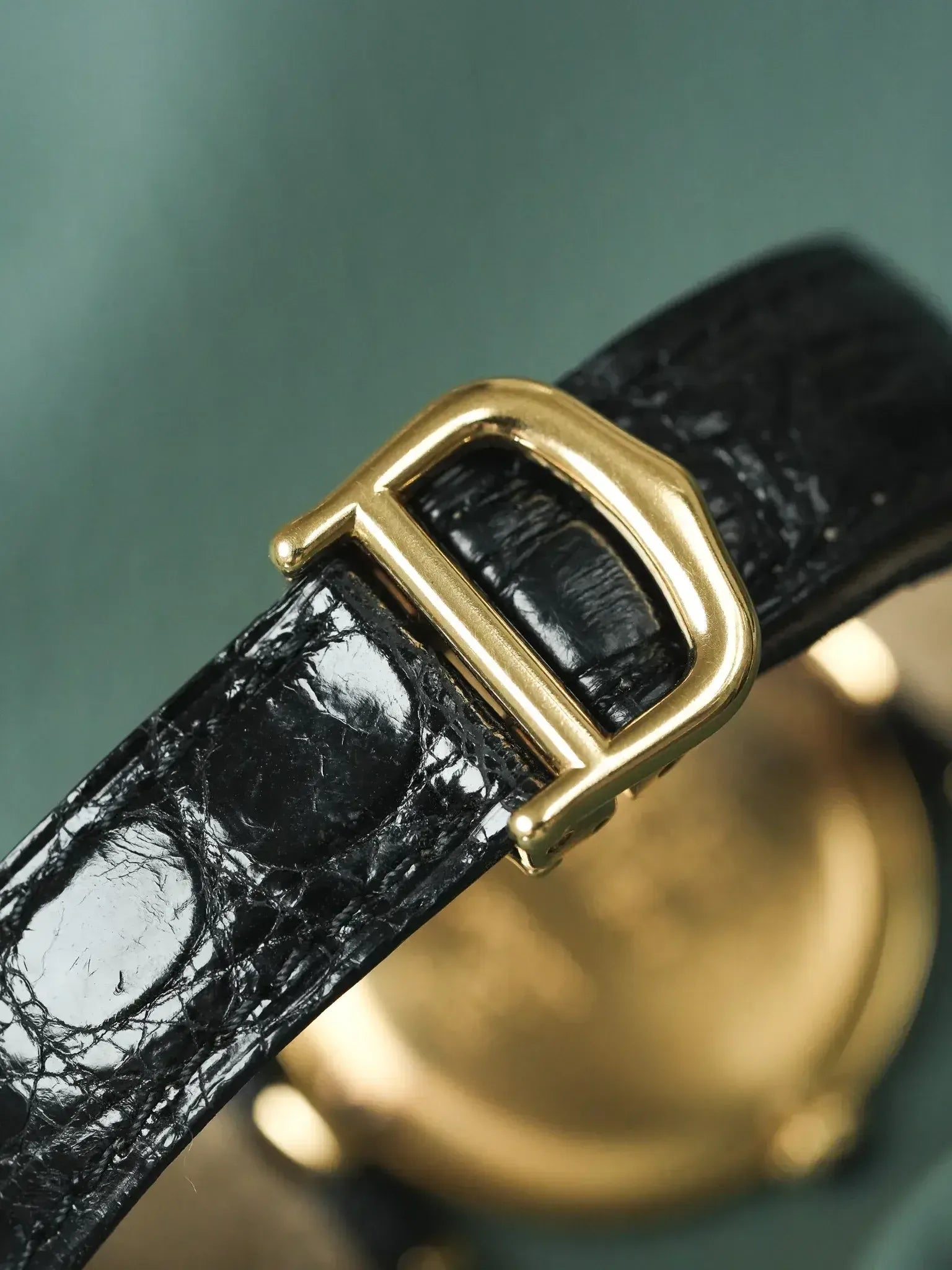 Vintage Cartier watch with black alligator strap and gold buckle on green background