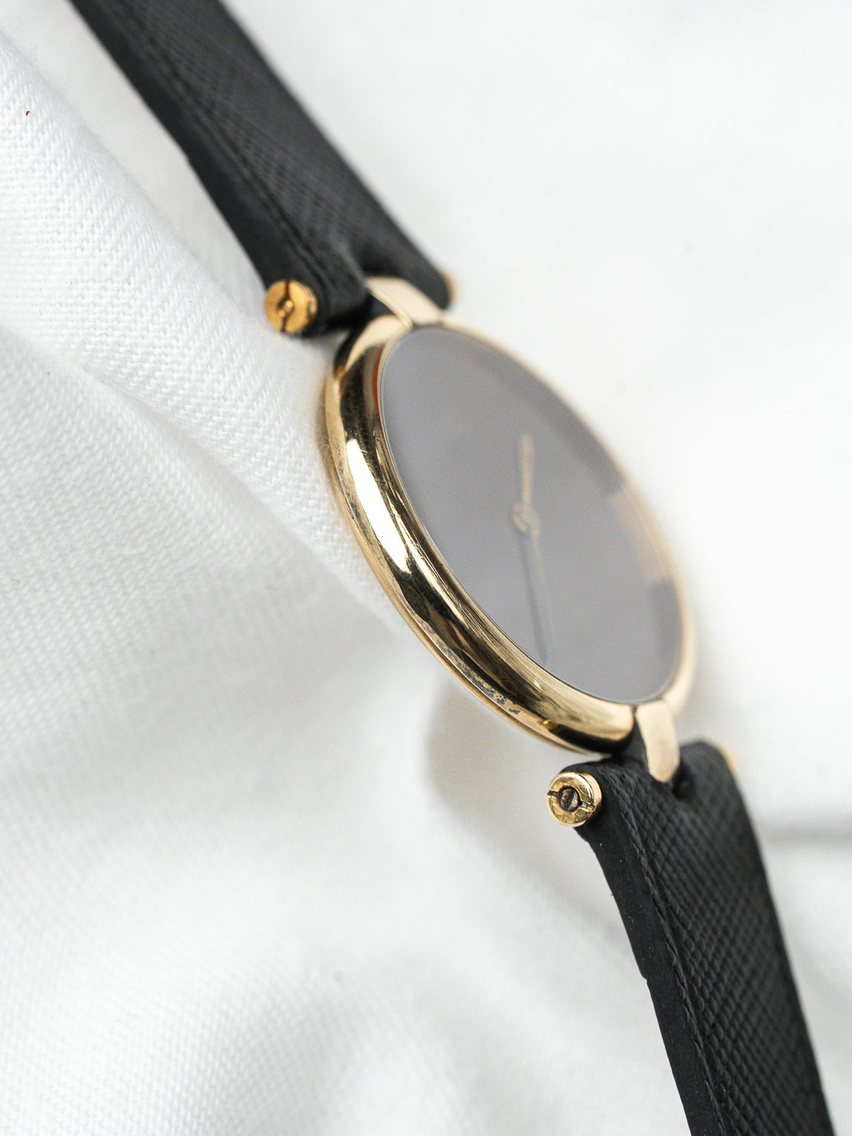 Montre vintage au boîtier rond doré, cadran sombre et bracelet en cuir noir