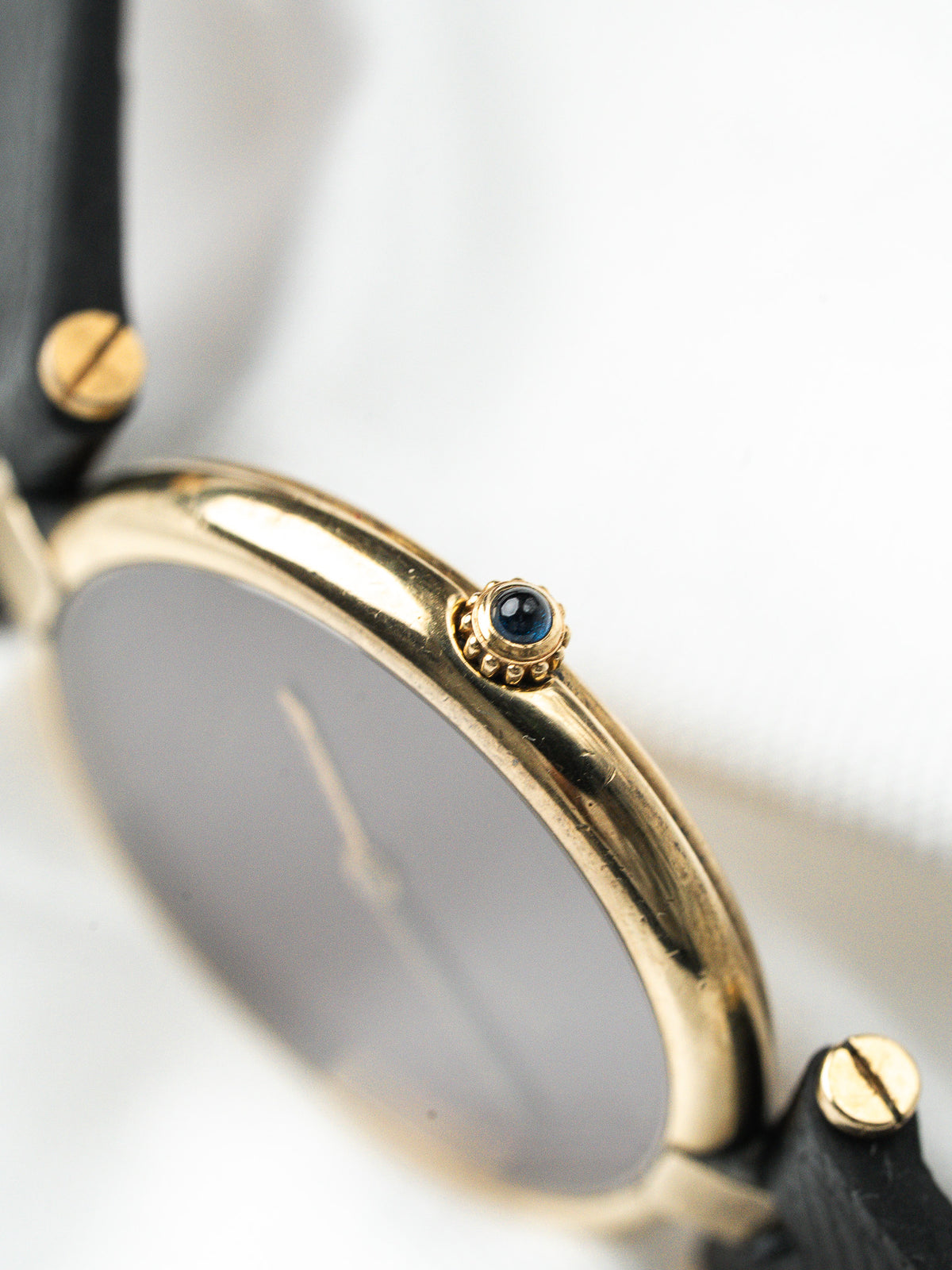 Détail d'une montre vintage en or avec couronne cabochon bleu et bracelet cuir noir