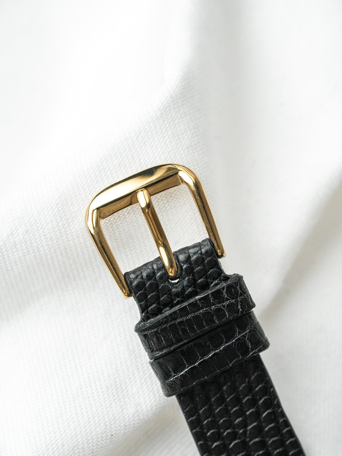 Boucle de bracelet de montre dorée sur cuir noir grainé, fond blanc neutre