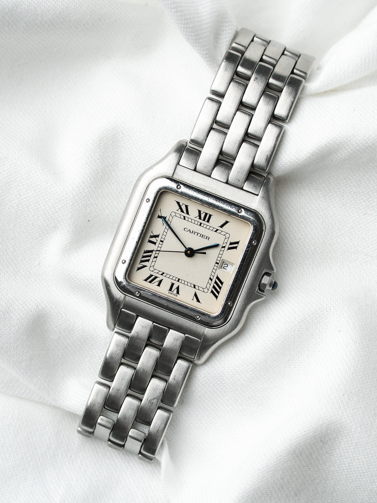 Montre Cartier vintage en acier, boîtier rectangulaire et cadran blanc sur fond textile