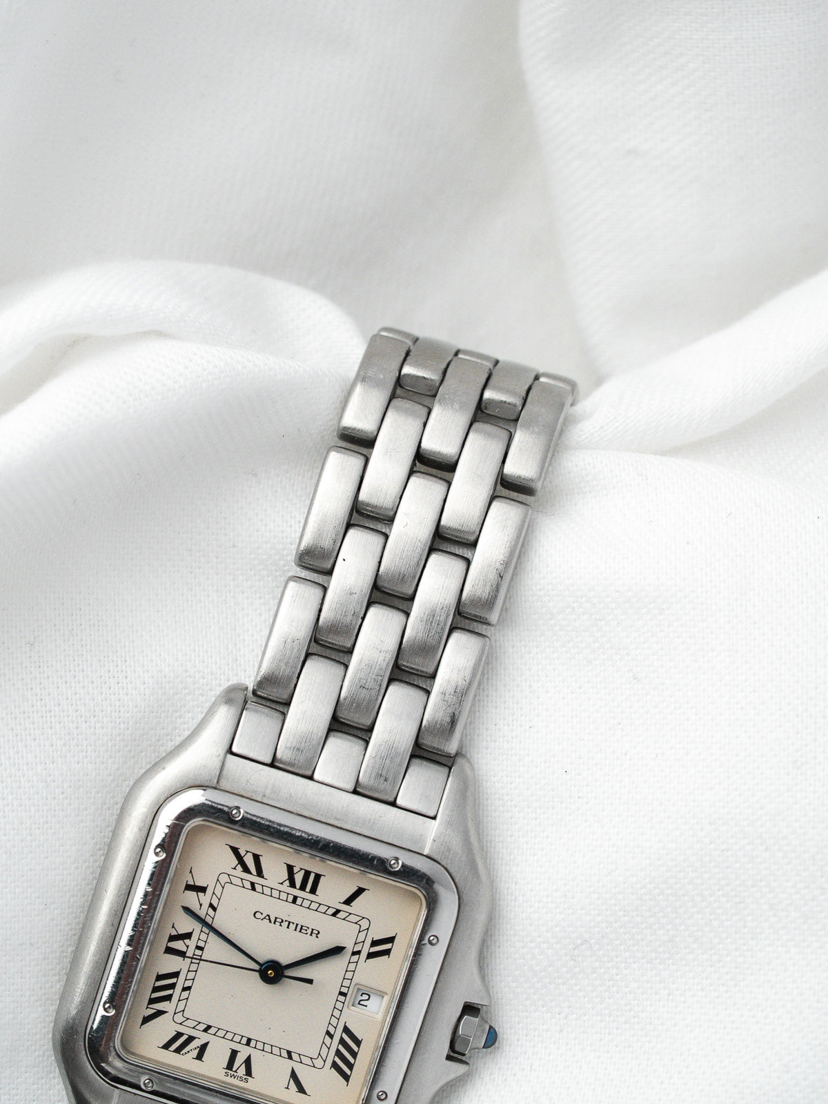 Montre Cartier vintage en acier avec boîtier rectangulaire et bracelet métallique sur fond blanc
