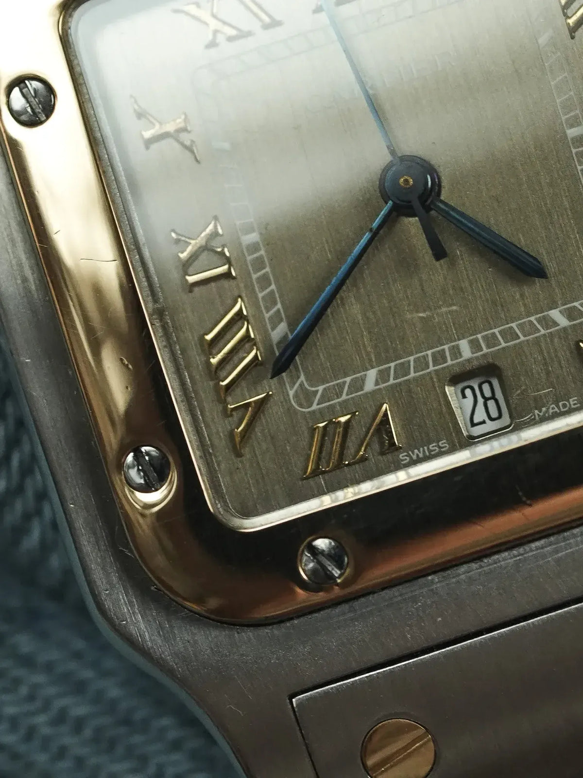 Cartier Tank watch with gold Roman numerals, blue hands, and date window on textured dial
