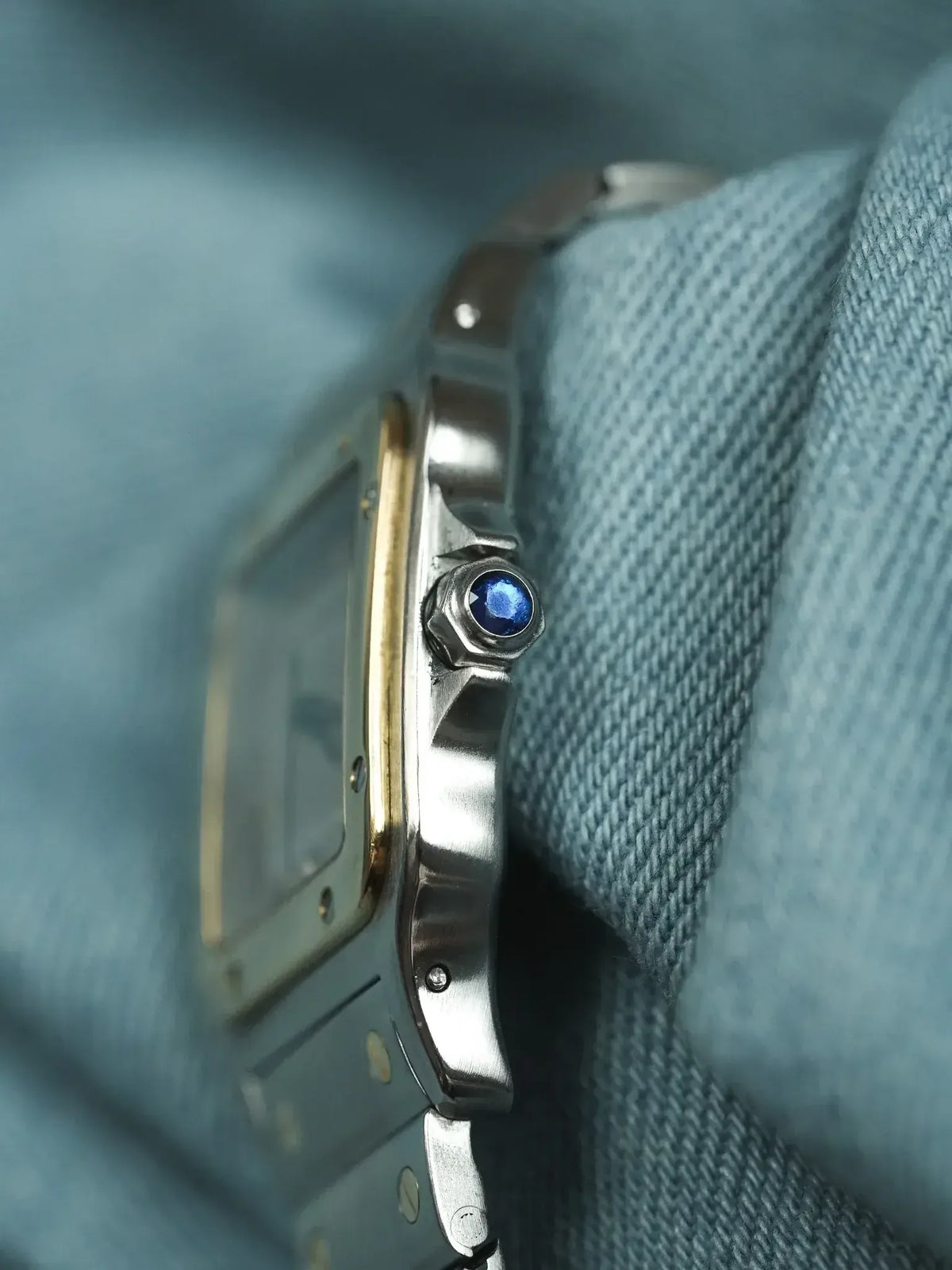 Cartier Santos watch with blue sapphire crown, steel and gold case, resting on denim