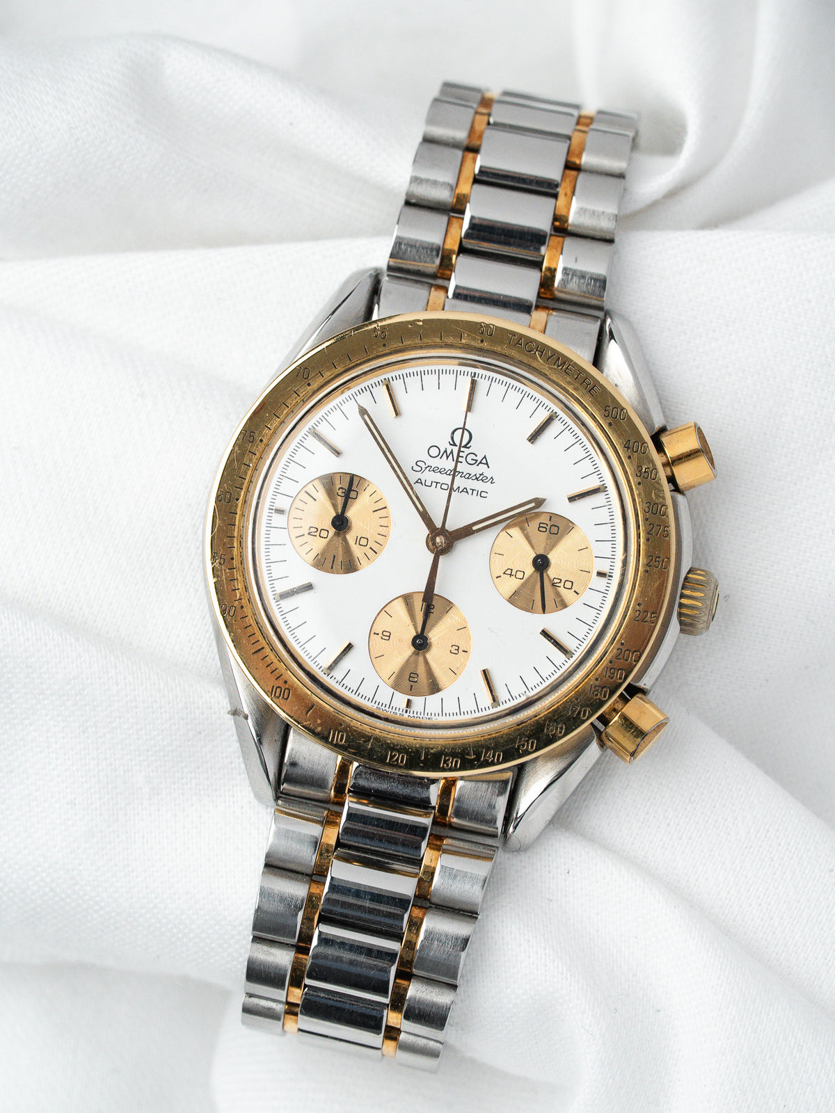 Omega Speedmaster vintage chronograph with white dial, gold accents, and two-tone bracelet on white fabric