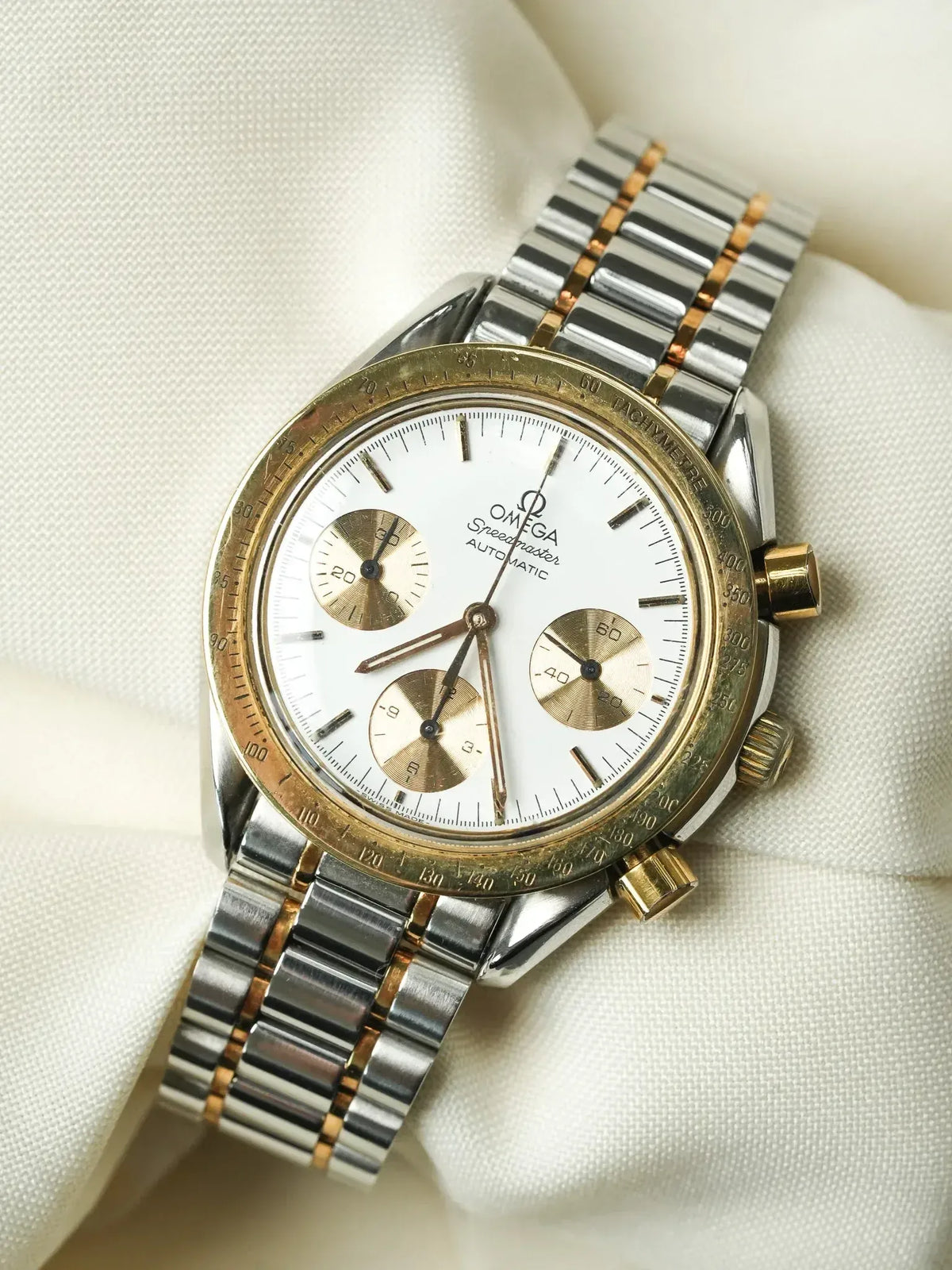 Omega Speedmaster vintage chronograph with white dial, gold subdials, and two-tone bracelet on fabric
