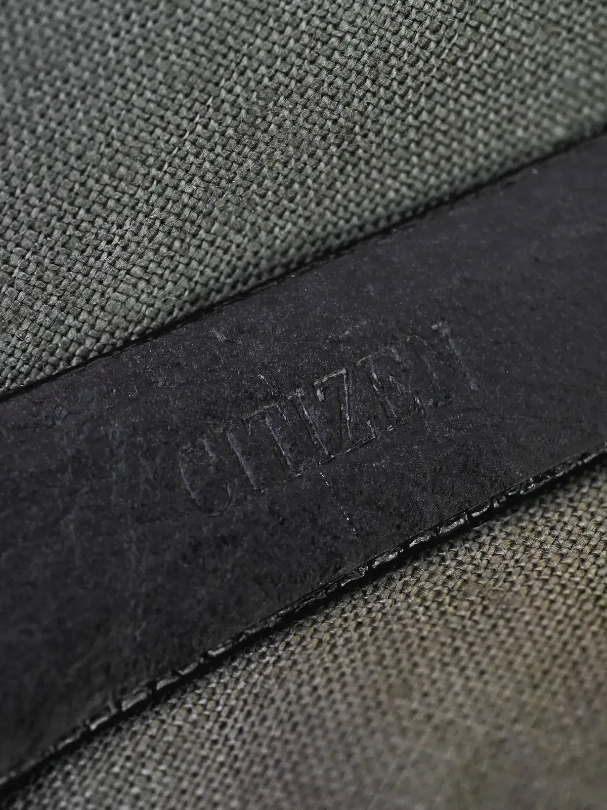 Citizen embossed on black leather strap against textured gray fabric