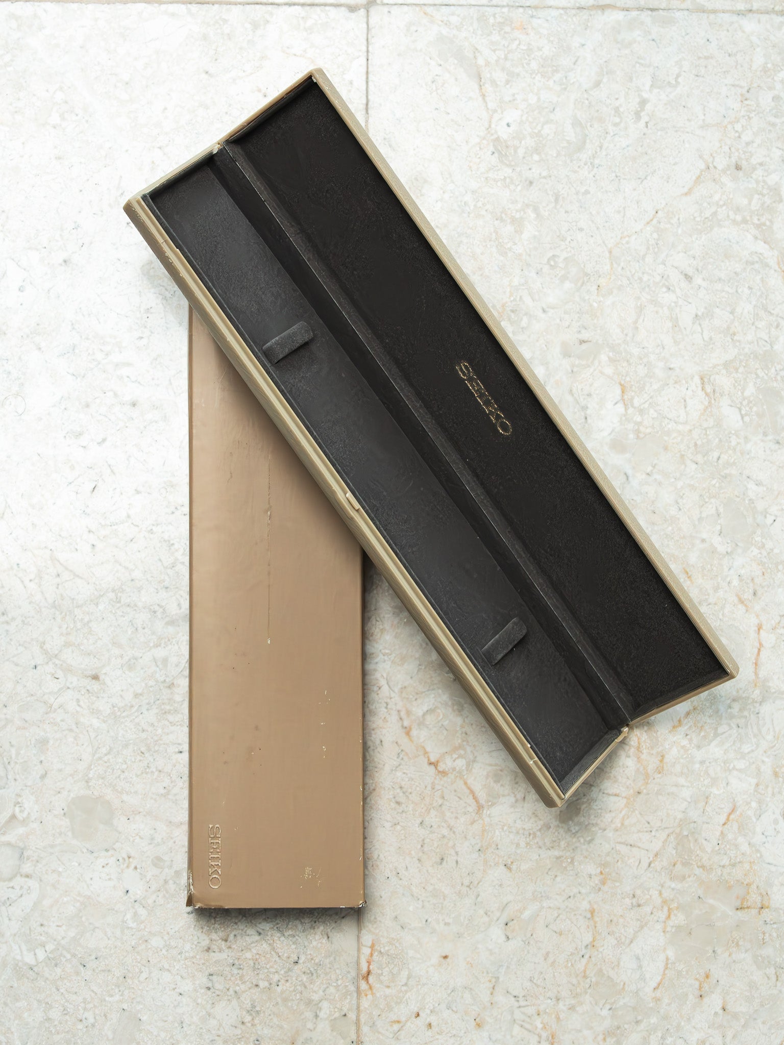 Vintage Seiko watch box with beige exterior and black velvet interior, open on marble surface