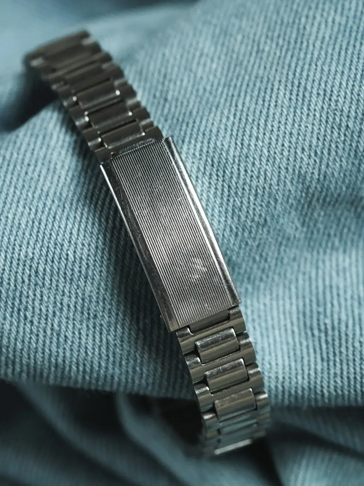 Vintage stainless steel watch bracelet with ribbed center link on denim background