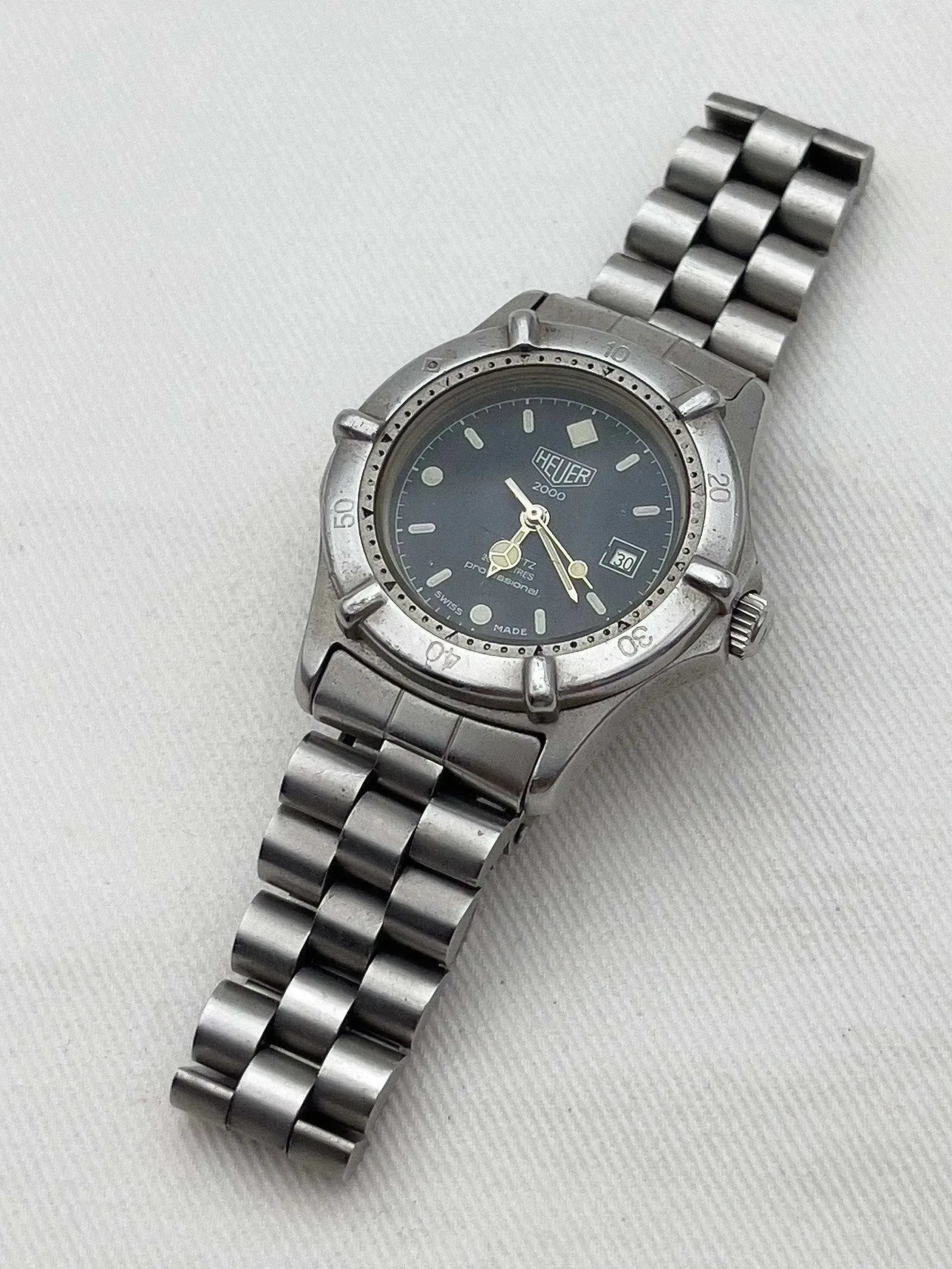 Heuer 2000 vintage watch with grey dial, steel bracelet, and rotating bezel on textured surface