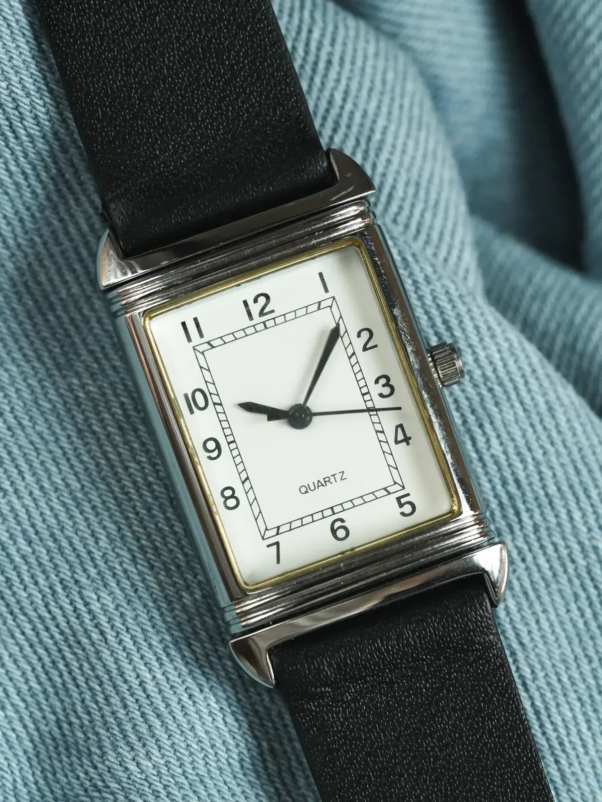Vintage quartz watch with rectangular silver case, white dial, black leather strap