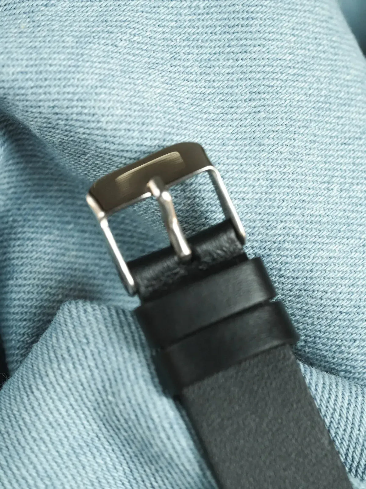Black leather watch strap with silver buckle on denim background