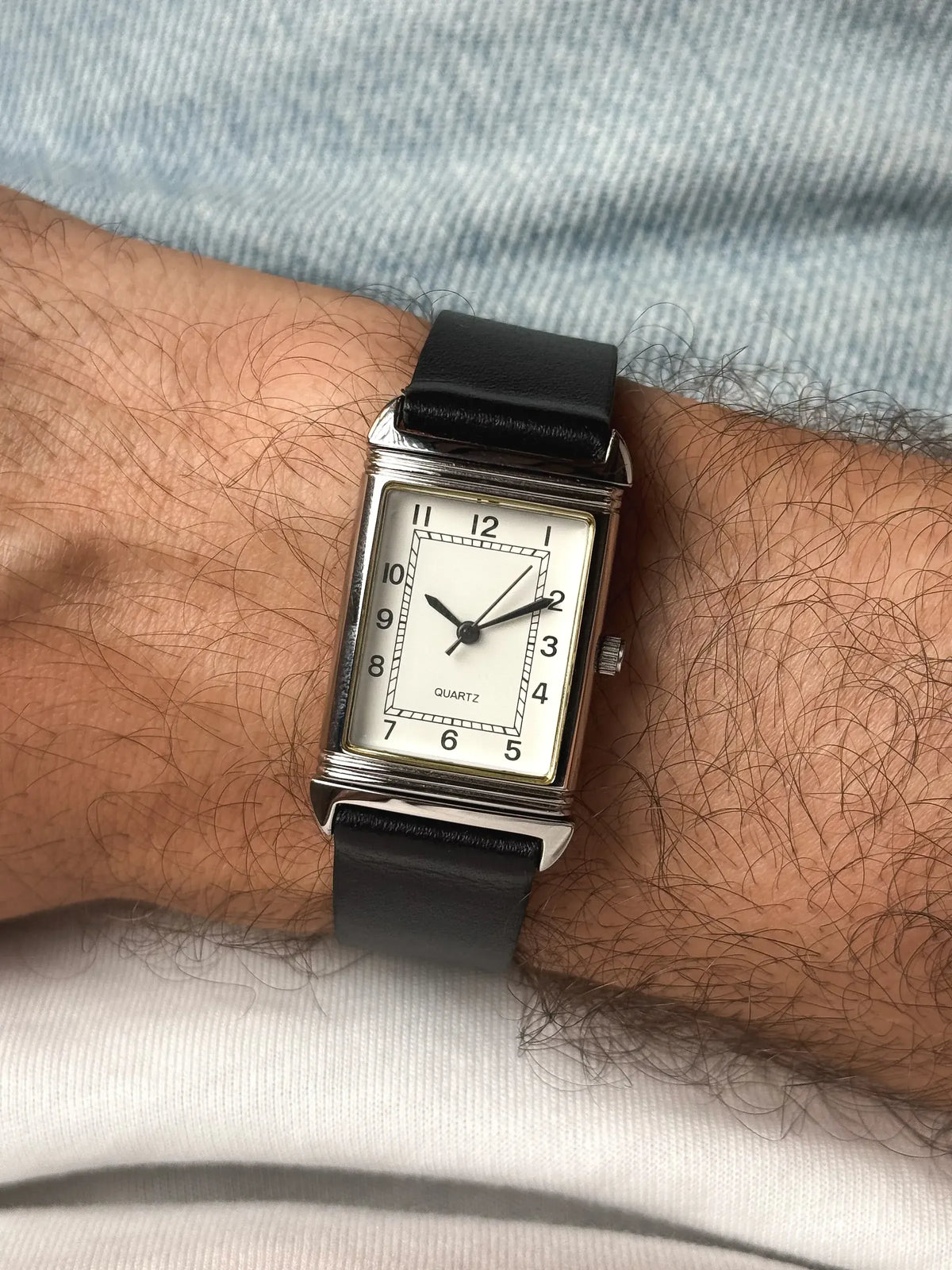 Vintage rectangular quartz watch with white dial, black leather strap, worn on wrist
