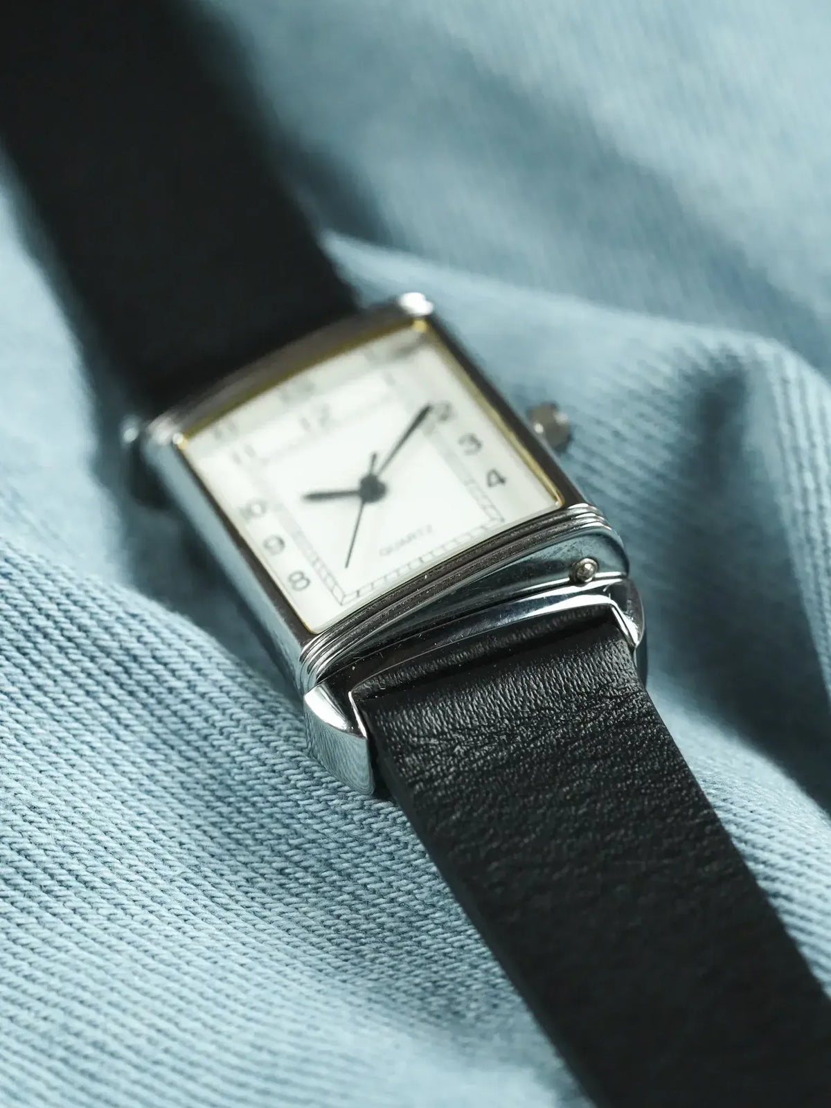 Vintage rectangular watch with white dial, black leather strap on blue fabric